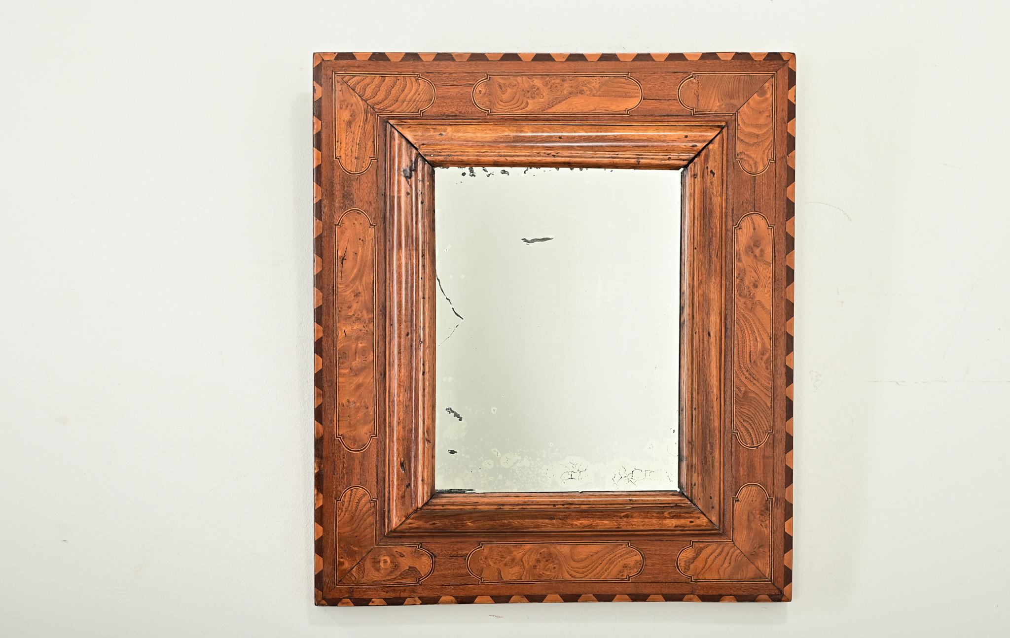 Straordinario specchio da parete francese dell'inizio del XIX secolo, intagliato a mano in mogano e noce burlato. Il bordo del pannello posteriore è smerlato con un'alternanza di pezzi curvi chiari e scuri, che si coordinano perfettamente con i