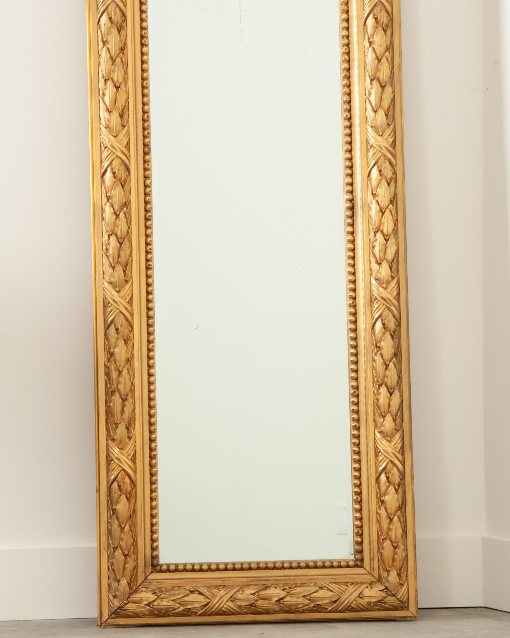 This elegant French 19th century gold gilt mirror is the perfect floor mirror for a smaller space. The beveled mirror plate is secured in a highly carved symmetrical frame, both are in wonderful antique condition with few signs of wear. Some foxing