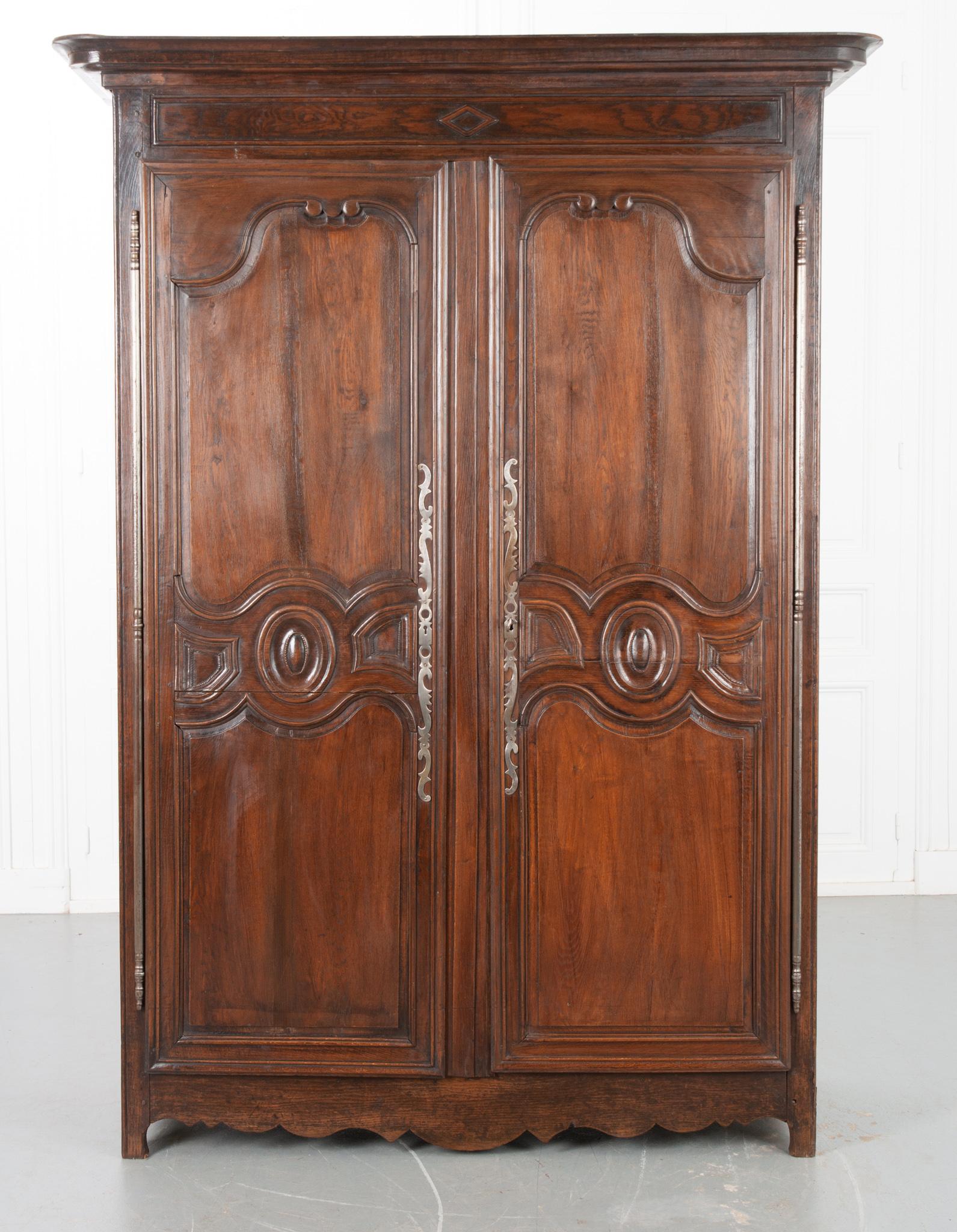 This solid oak armoire from 19th century France is substantial in size and full of hand-carved detail. A large cornice tops the piece above a carved diamond detail. The large doors feature shaped panels with beautiful carving and impressive linear