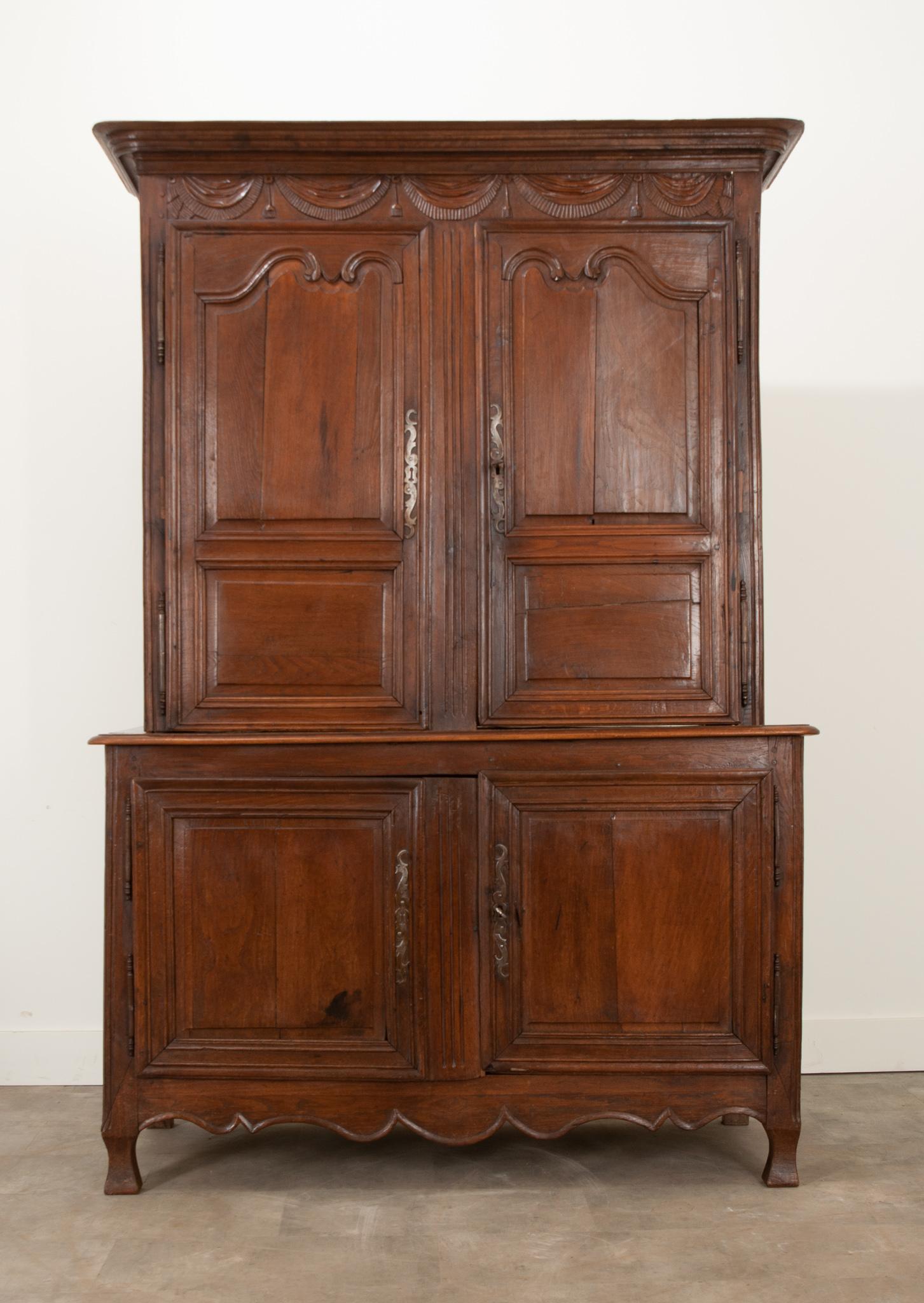 A handsome and sizable solid oak buffet a’ deux corps with Provincial charm from 19th century France. This four door case antique is split into two bodies: a larger lower body and a smaller upper body. The upper is crowned with an molded cornice