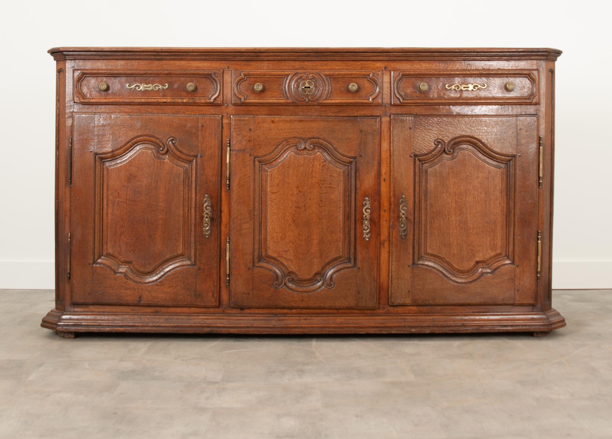 A substantial solid oak enfilade from the 1800's France. The entire case piece is made of solid carved oak and has a warm patina. All three drawers are cleaned and slide with ease using brass knobs. The paneled doors open on brass hinges to their