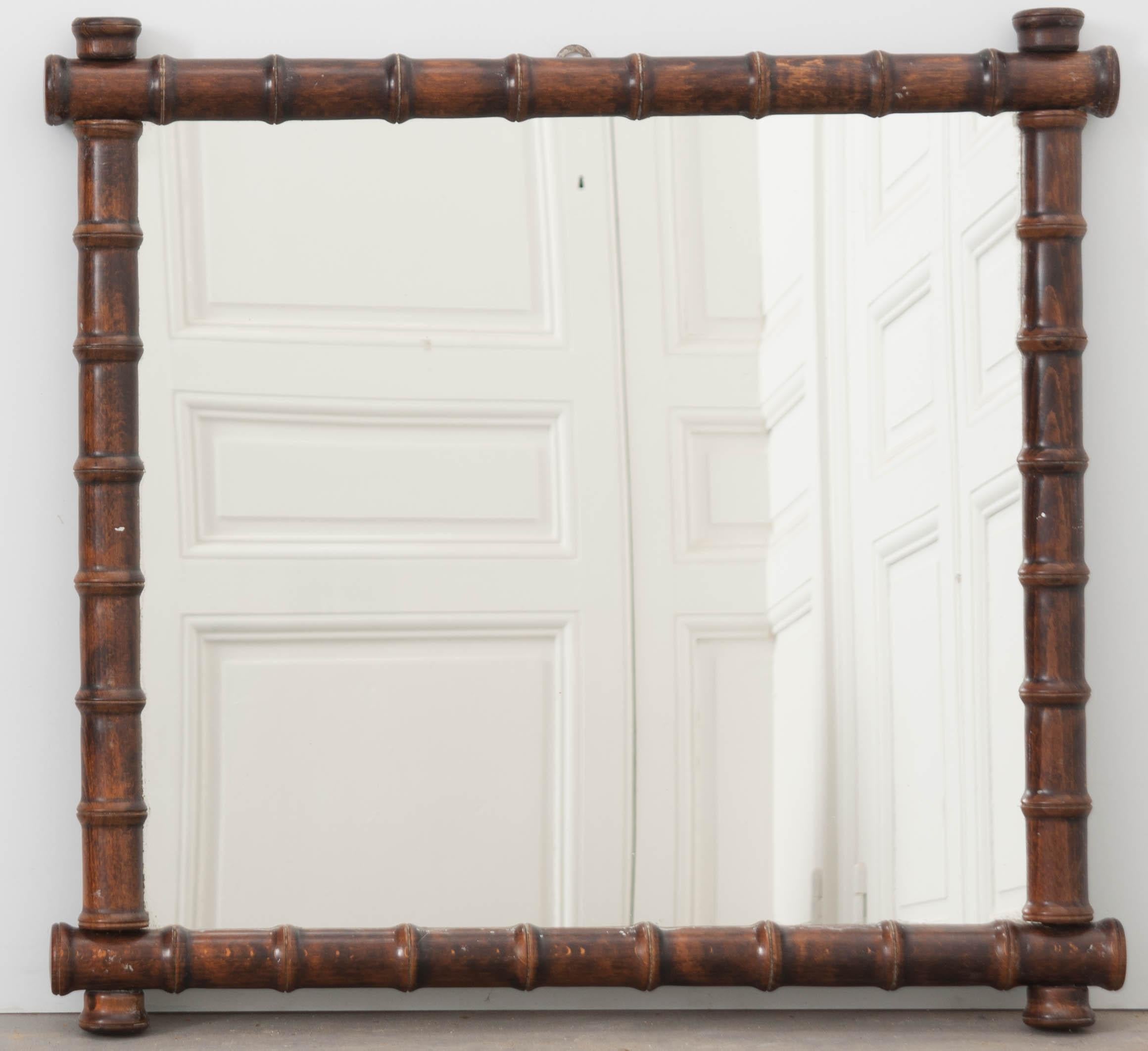 This terrific faux bamboo mirror was made in France, circa 1880. Its frame was made by turning hand-selected oak into a stacked-spool or faux bamboo design. The darker frame is nearly a square, which is a somewhat unusual shape for these mirrors.