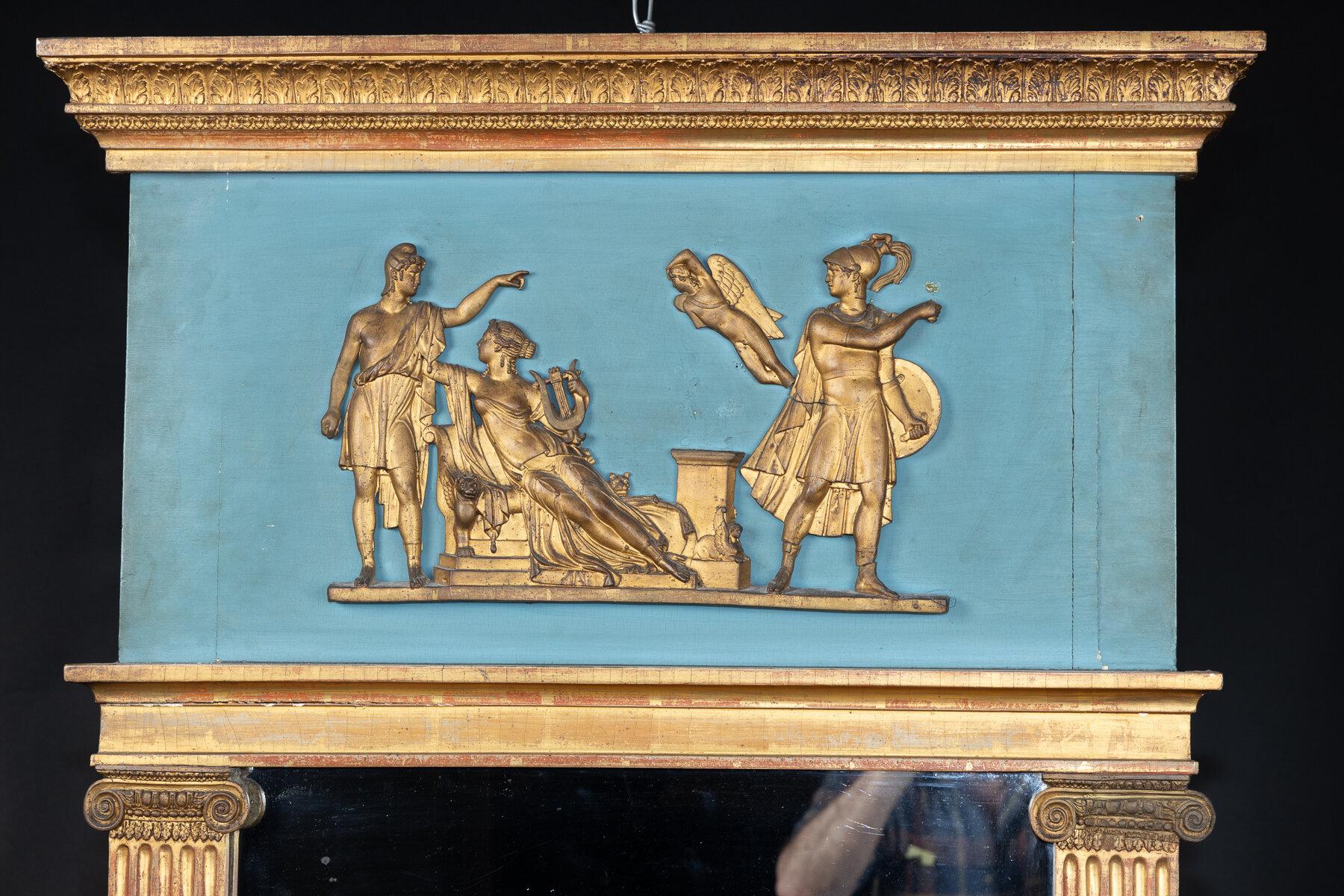 Trumeau français du XIXe siècle, sculpté, peint et doré, de style Empire ou néo-classique, avec un fond bleu et des figures allégoriques dorées. Les personnages reposent sur un fronton supérieur composé de feuilles sculptées et dorées. Un pilastre
