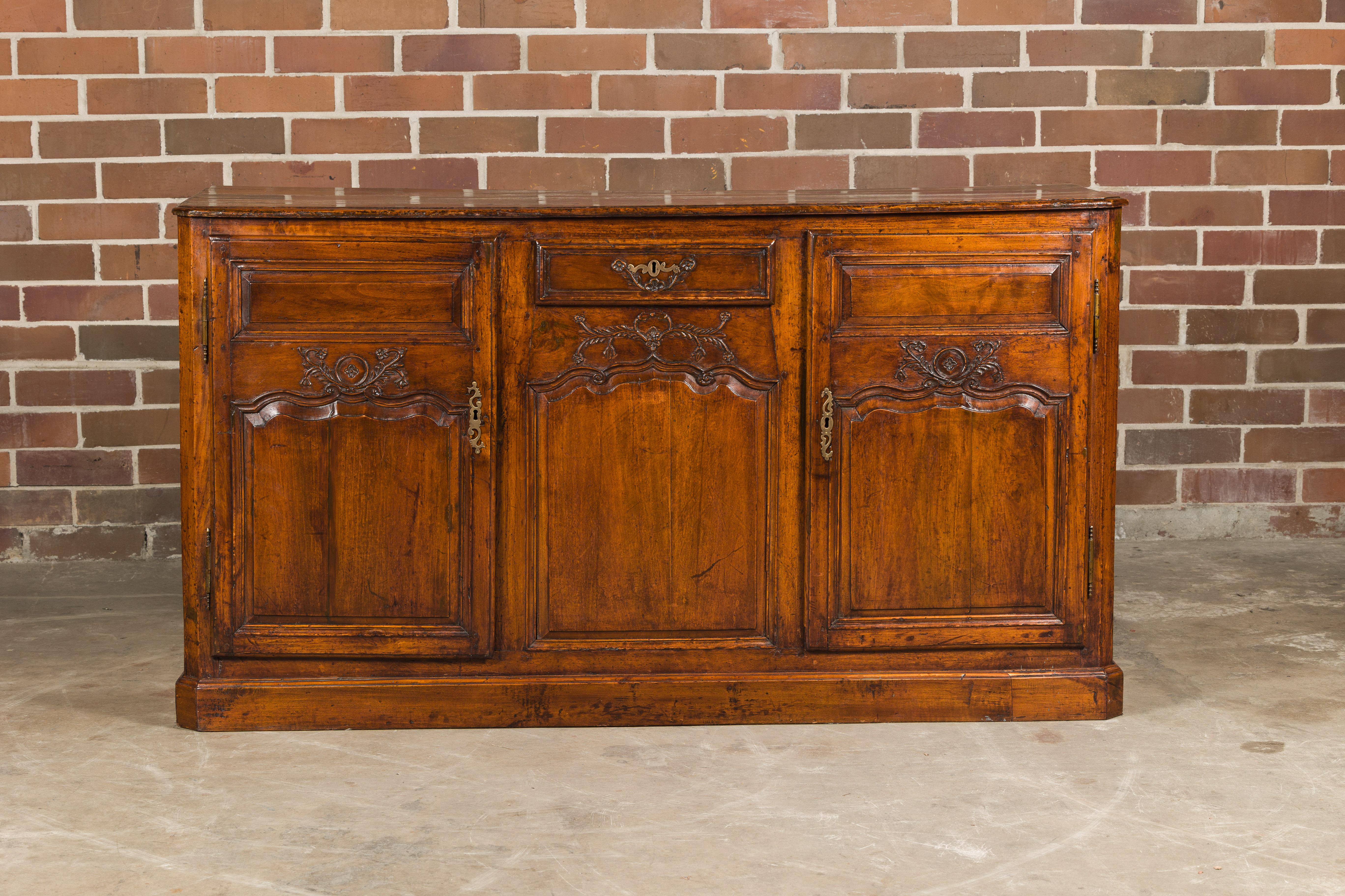 A French walnut buffet from the 19th century with two doors, a single drawer and carved foliage décor. Indulge in the timeless elegance of this French walnut buffet from the 19th century, a piece that marries classic design with exquisite