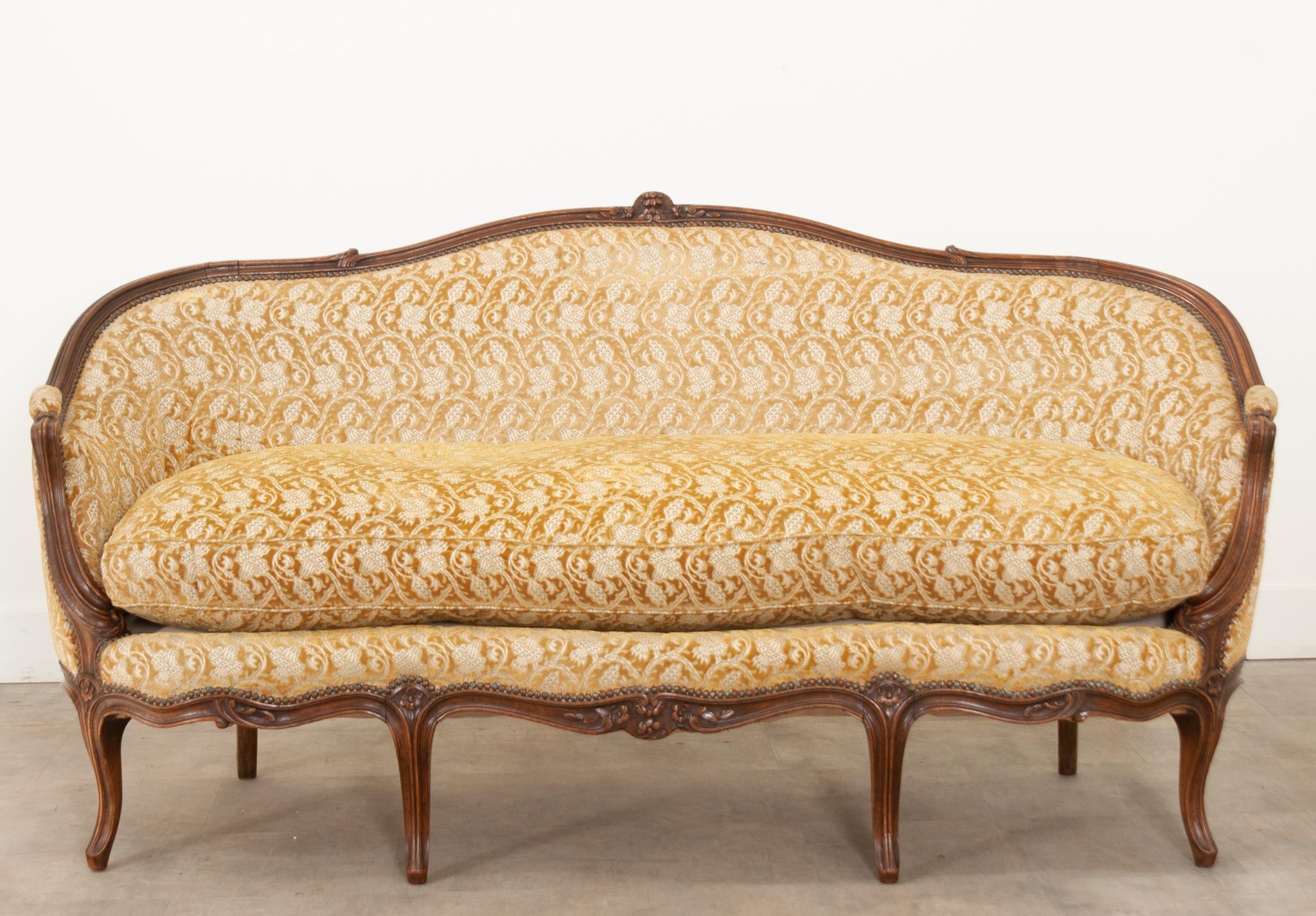 This elegant and comfortable settee was crafted in 19th century France and features beautiful cut velvet upholstery in a gorgeous botanical print and goldenrod color.  The carved walnut frame is rich in tone and has deep curving trim, florals, and