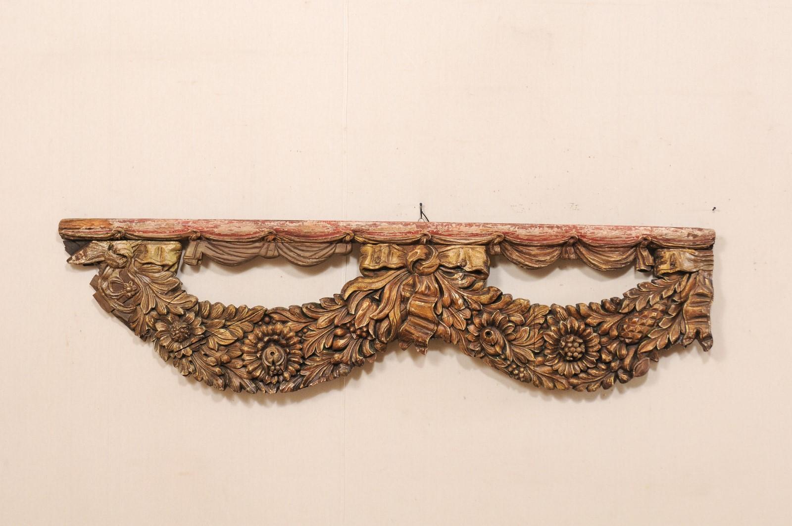 A French carved wood fragment from the early 19th century. This antique wall decoration from France has an overall oblong, just shy of 6.5 feet in length, having a horizontally positioned shape, with a level, wooden top rail draped with several