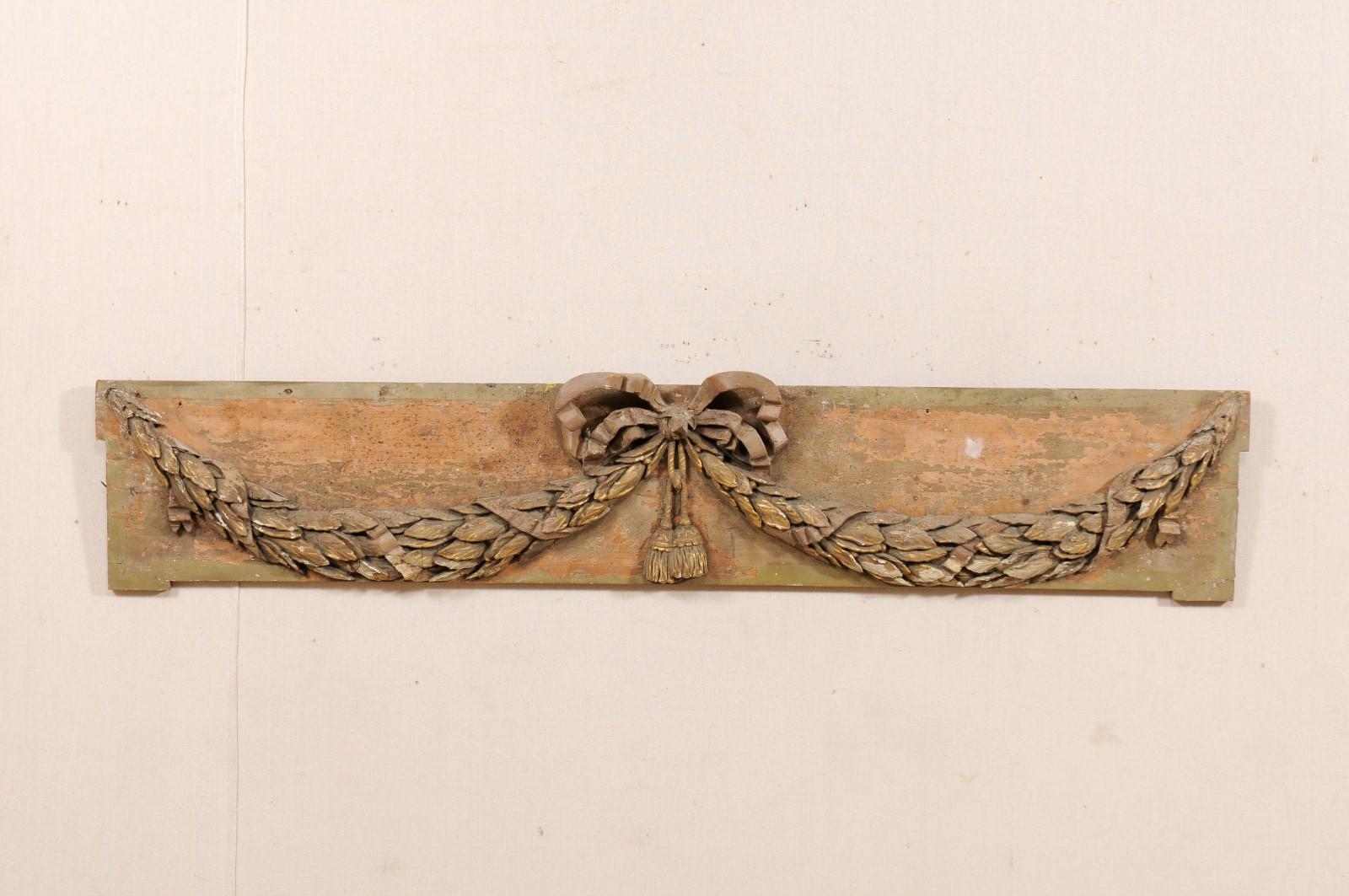 A French 19th century wood carved decorative hanging wall plaque. This antique wall ornament from France features a rectangular-shaped plaque with a three-dimensional, hand-carved swagged wreath, gathered in the center with a bow and carved tassels