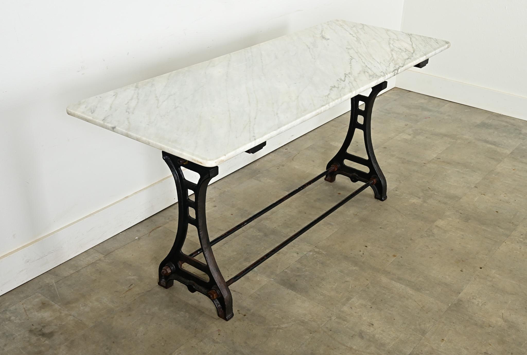 An exceptional French bistro dining table with industrial details in the cast iron base, recalling the profile of the Eiffel Tower. The white marble slab has a patinated and etched surface, consistent with age and type of use, over light gray