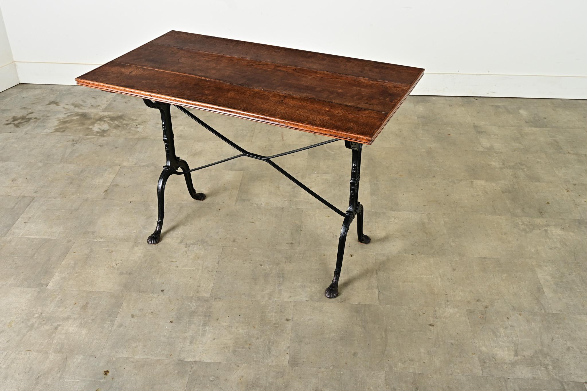 Une table de bistrot française exceptionnelle avec des détails d'époque Beaux Arts dans la base en fonte. Le plateau en chêne foncé présente une surface bien patinée, conforme à l'âge et au type d'utilisation, remarquable par le bandeau décoratif