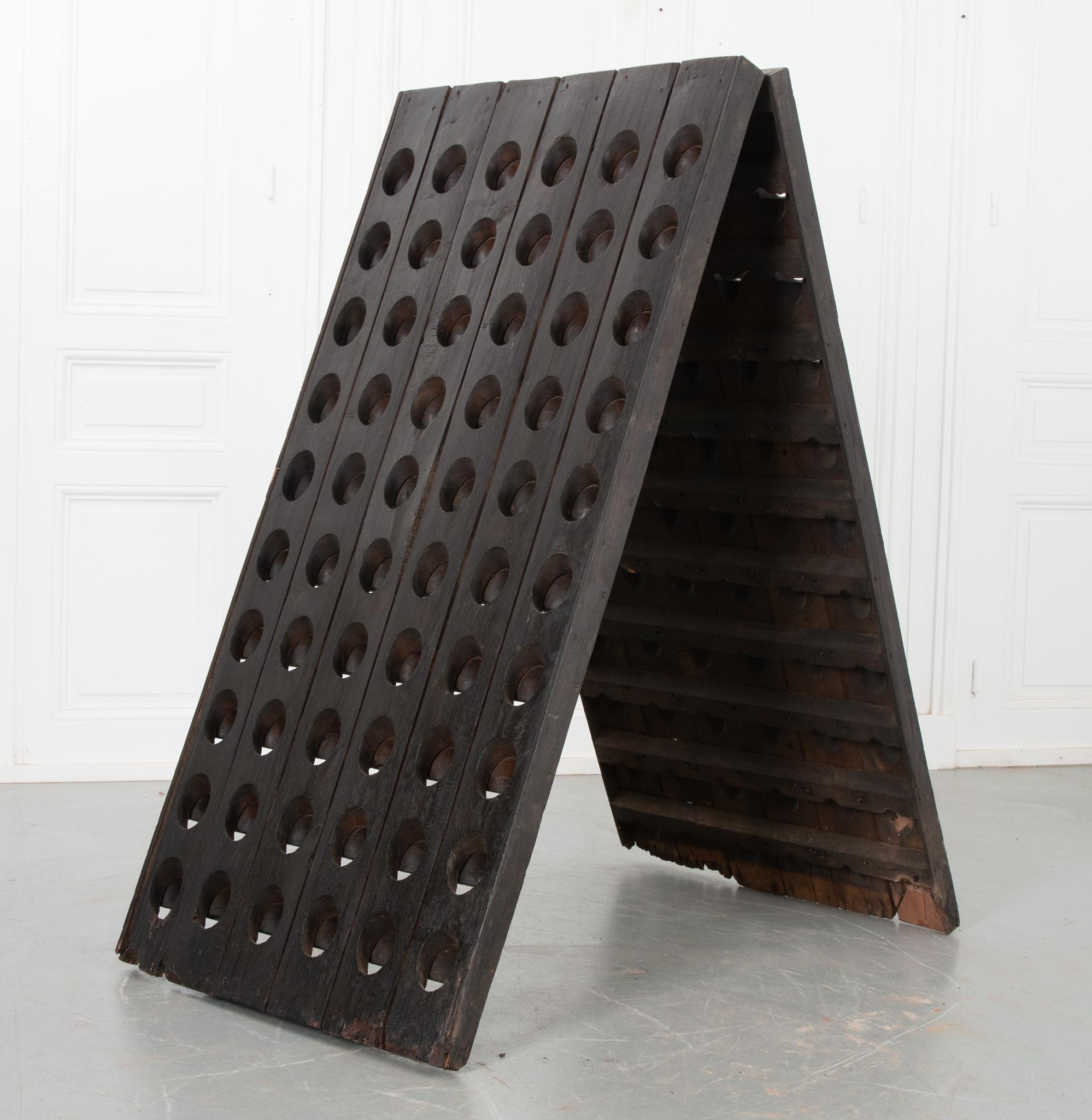 This is a riddling rack, a standing wooden A-frame rack that’s used in the process of making champagne. It has 120 holes that secure the bottles by the neck at an angle. This is one of the best ways to display a large selection of wine bottles. The
