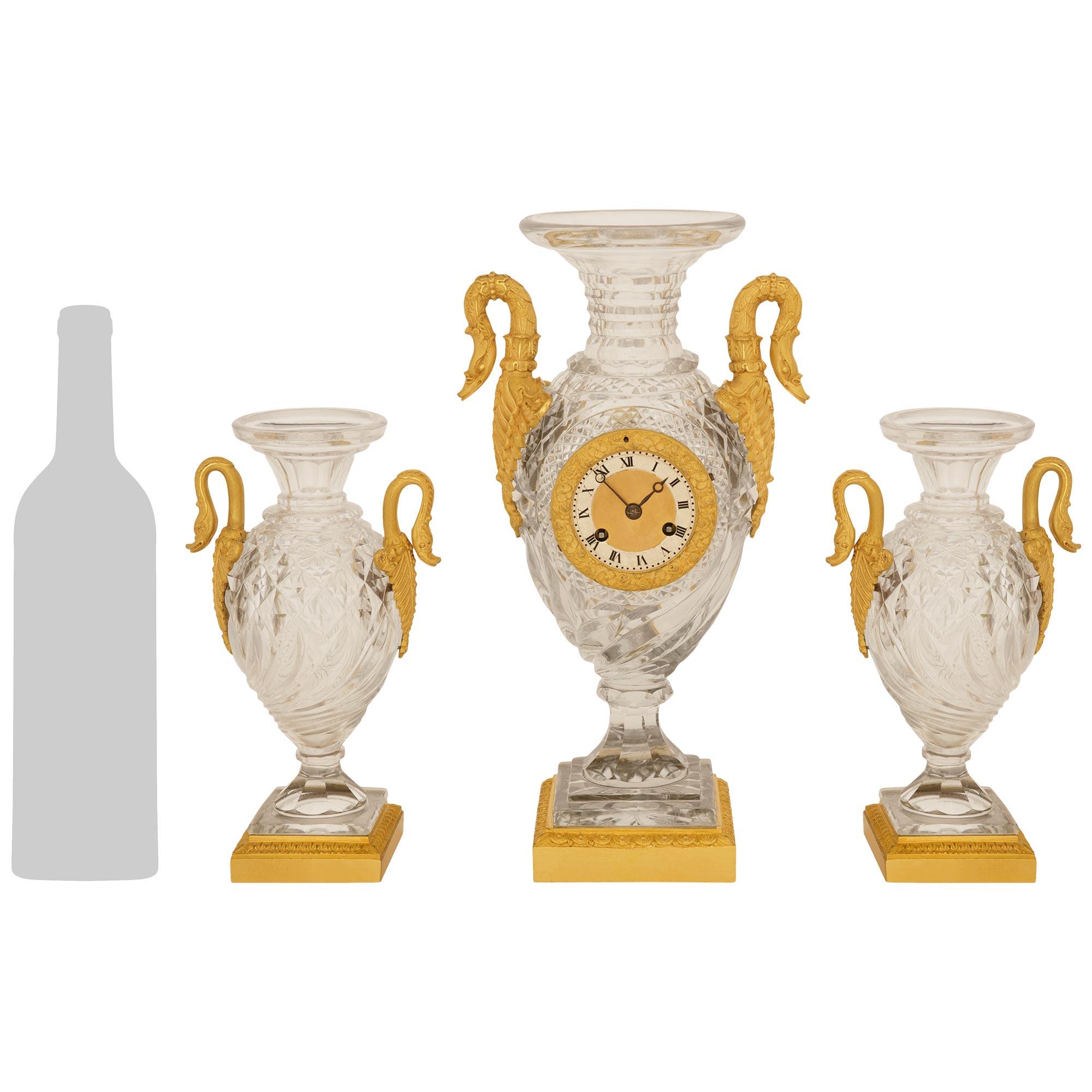 An elegant and high quality French 19th century Charles X Period Baccarat Crystal and Ormolu garniture set. This wonderful garniture set consists of a clock and pair of urns, raised by Ormolu plinths bordered at the top by a Rais-de-Coeur band and