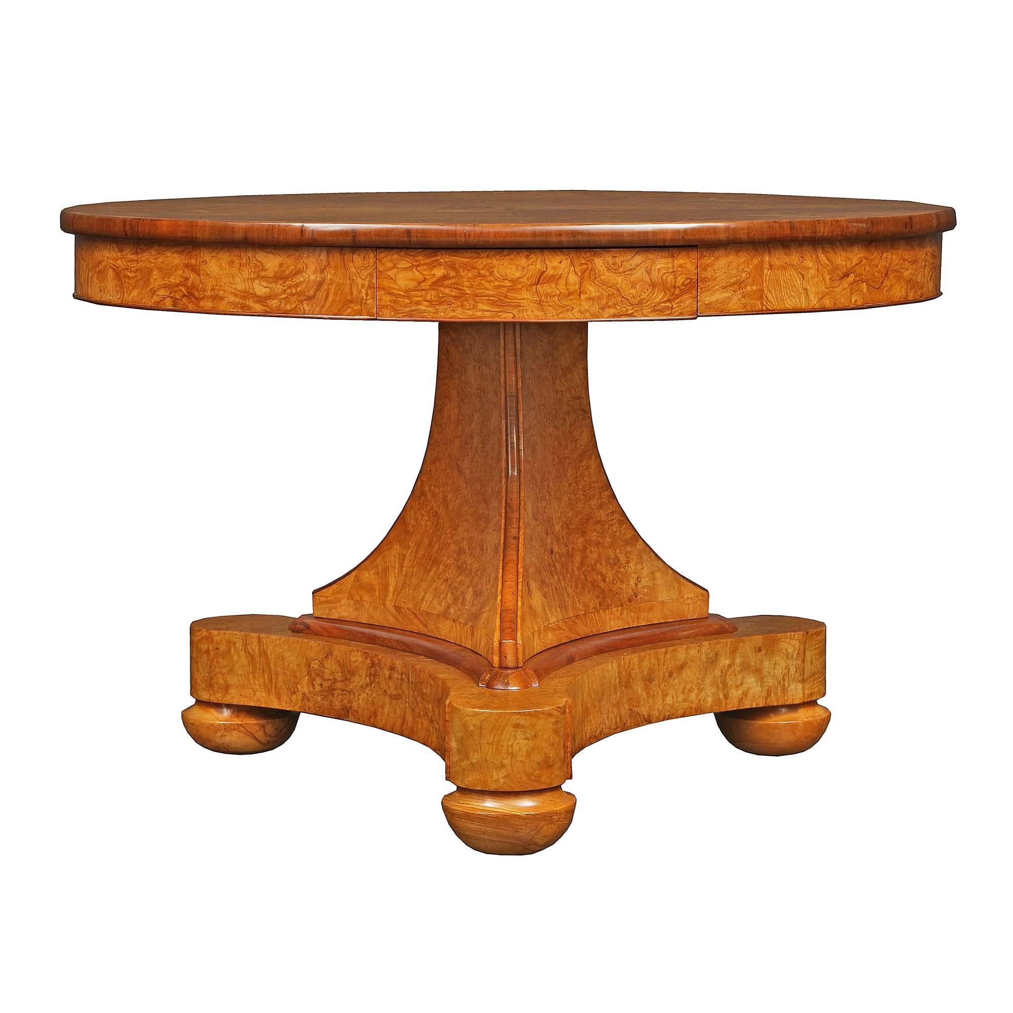 A very attractive French 19th century Charles X st. burl walnut center table. The table is raised on bun feet below a triangular base with concave sides. A central triangular supports the circular top. At the full apron are two drawers below the