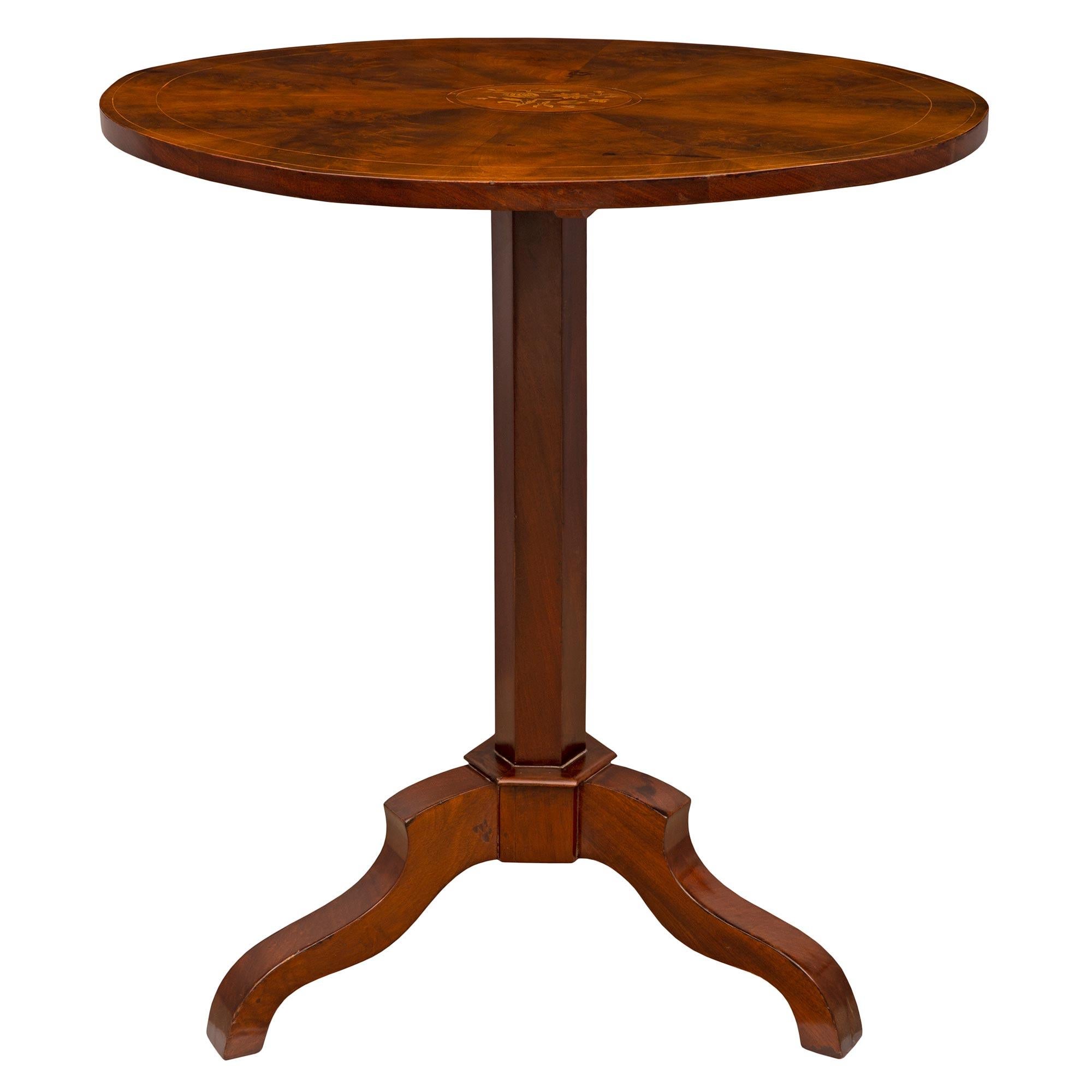 An elegant and small scale French 19th century Charles X period flamed Mahogany and Tulipwood tilt top side table. The circular table is raised by three finely scrolled supports joined at a hexagonal reserve and central support. The top tilts up via