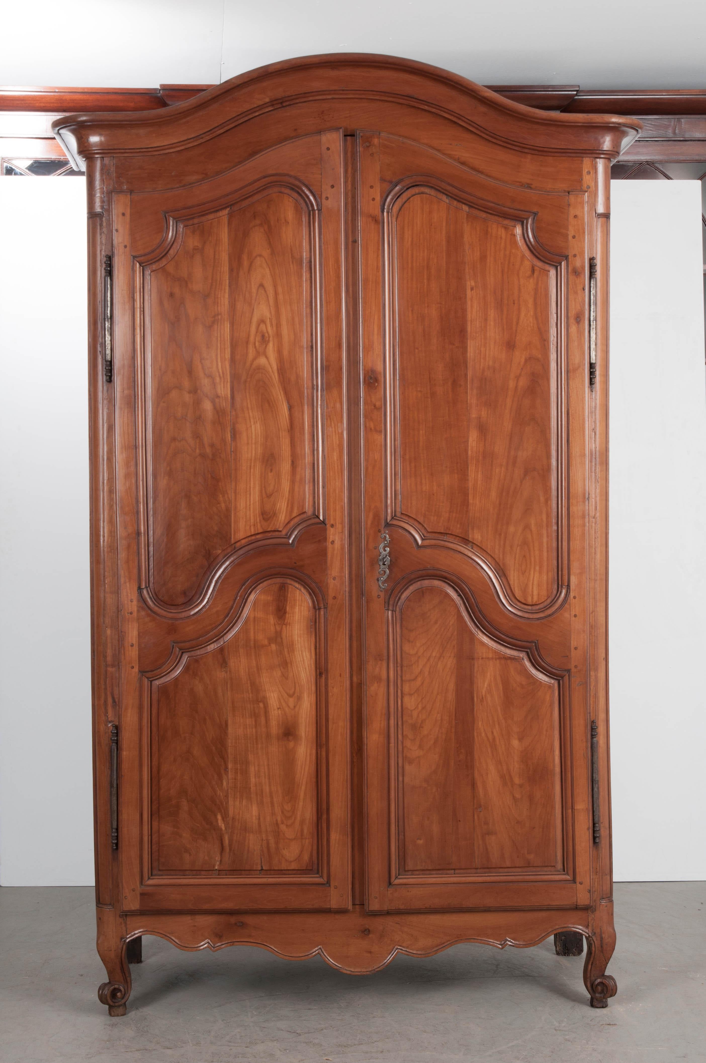 A Chapeau de Gendarme cornice crowns this 19th century, French, Louis XV style cherry armoire. Two large doors with shapely carved panels create a gorgeous façade to this solid-cherry antique. They are hung on steel barrel hinges, have styled