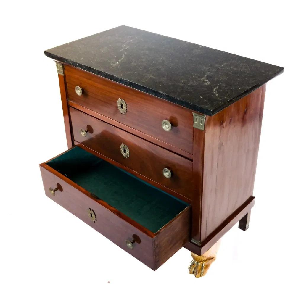 A French Empire Period Fruitwwod commode or chest of drawers  of rectangular shape, the three drawers raised on gilt wood paw feet, with Empire bronze escutcheons and pulls , having quarter columns with bronze capitals and a black marble