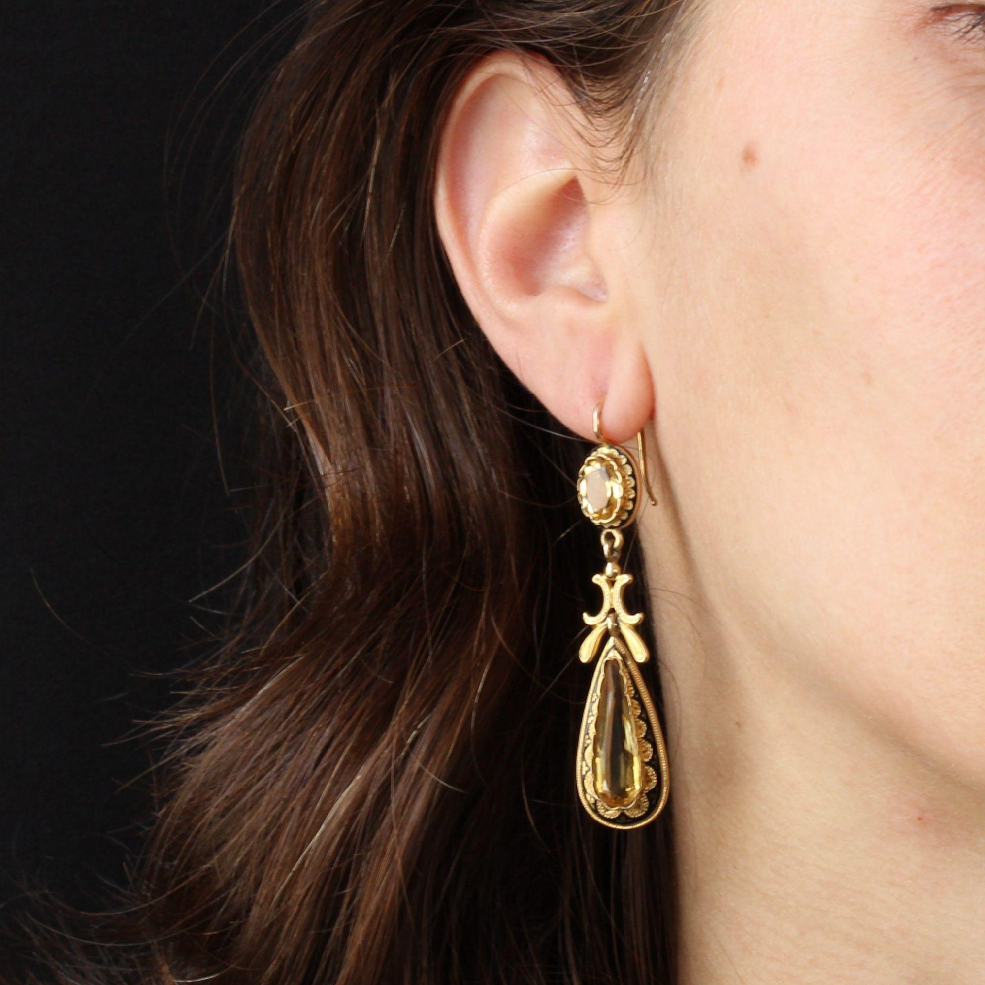 For pierced ears.
Earrings in 18 karat yellow gold, horse head hallmark.
Each antique earring is made of a citrine in polylobate setting, surrounded by small petals chiseled on a black enamel. It holds in tassel a long drop of citrine of the same