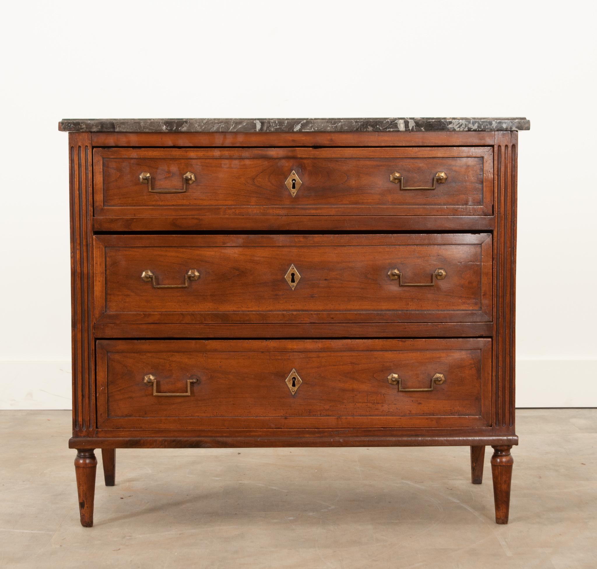 A petite French commode in the Louis XVI Style is cleaned, polished and ready for the next generation of owners. The original saint anne marble sits on the simple solid walnut frame and has three graduating drawers all with brass drawer pulls and