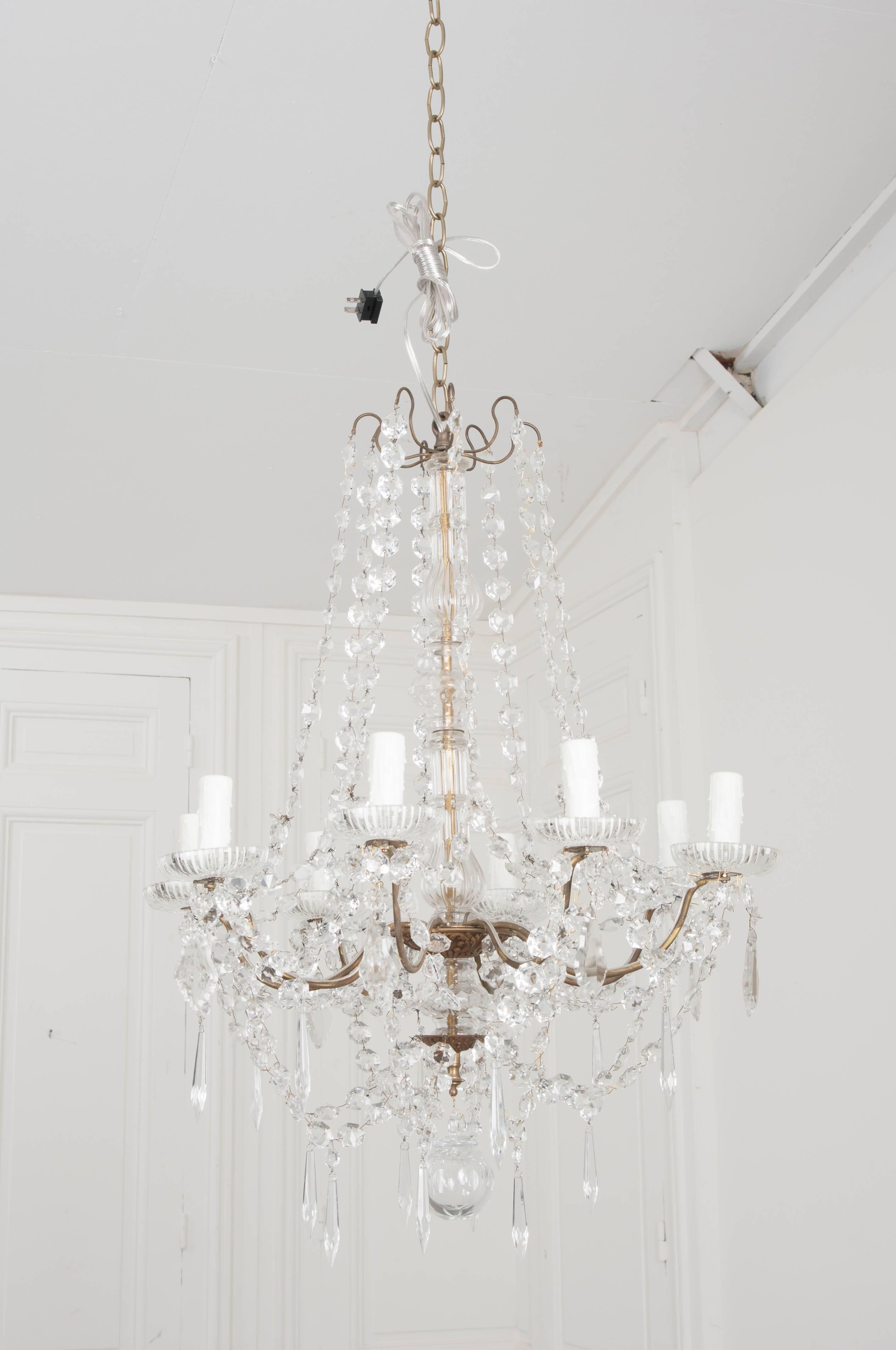 An exceptional late 19th century French eight-light crystal and brass chandelier. The light has a slender brass frame, from which crystal garlands and chains hang, supporting and beautifying the antique. The central column is encased in blown glass