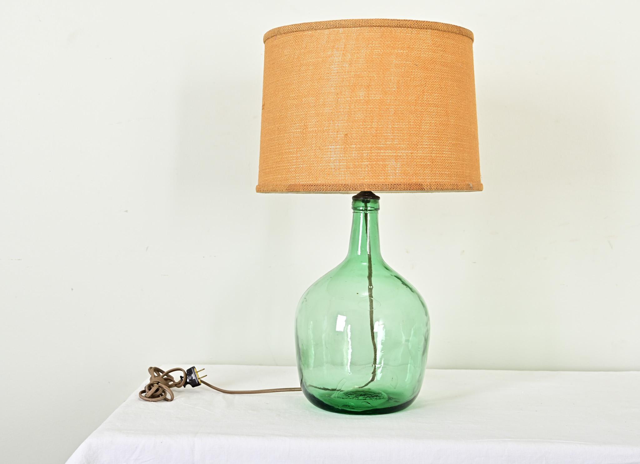 This 19th century French green glass demijohn for storing wine was given a creative update as a table lamp base. The light from the standard-base bulb softly illuminates the bottle to reveal all the texture of the handmade glass. Burlap fabric on