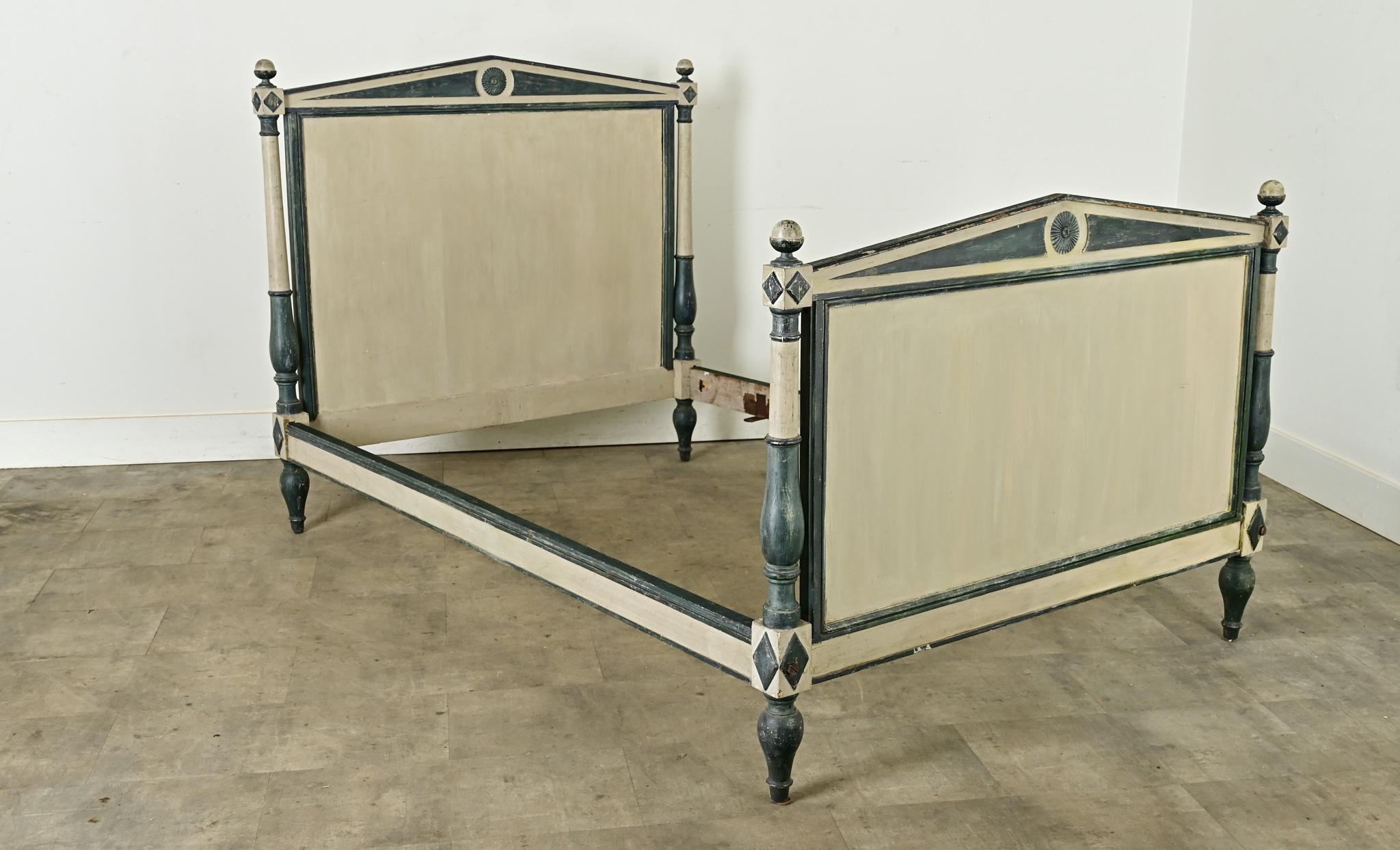 A French 19th century bed from the Directoire period with a warm gray and French blue color scheme. Both the headboard and the footboard have a low and wide pitch across the top to form a kind of pediment recalling Neoclassical architecture. Four