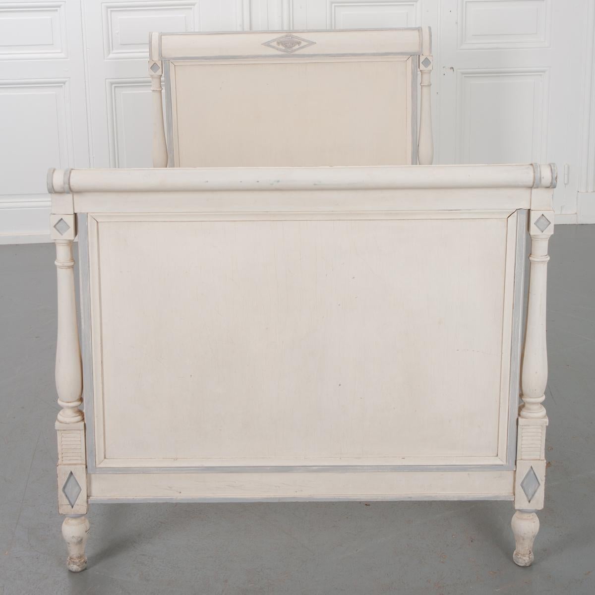 This elegant, 19th century bed is in the Directoire style. It has a pale gray paint with a blue-gray accent highlighting the details. The headboard and footboard have columns on each side and are centered by a hand carved diamond with an urn in it.