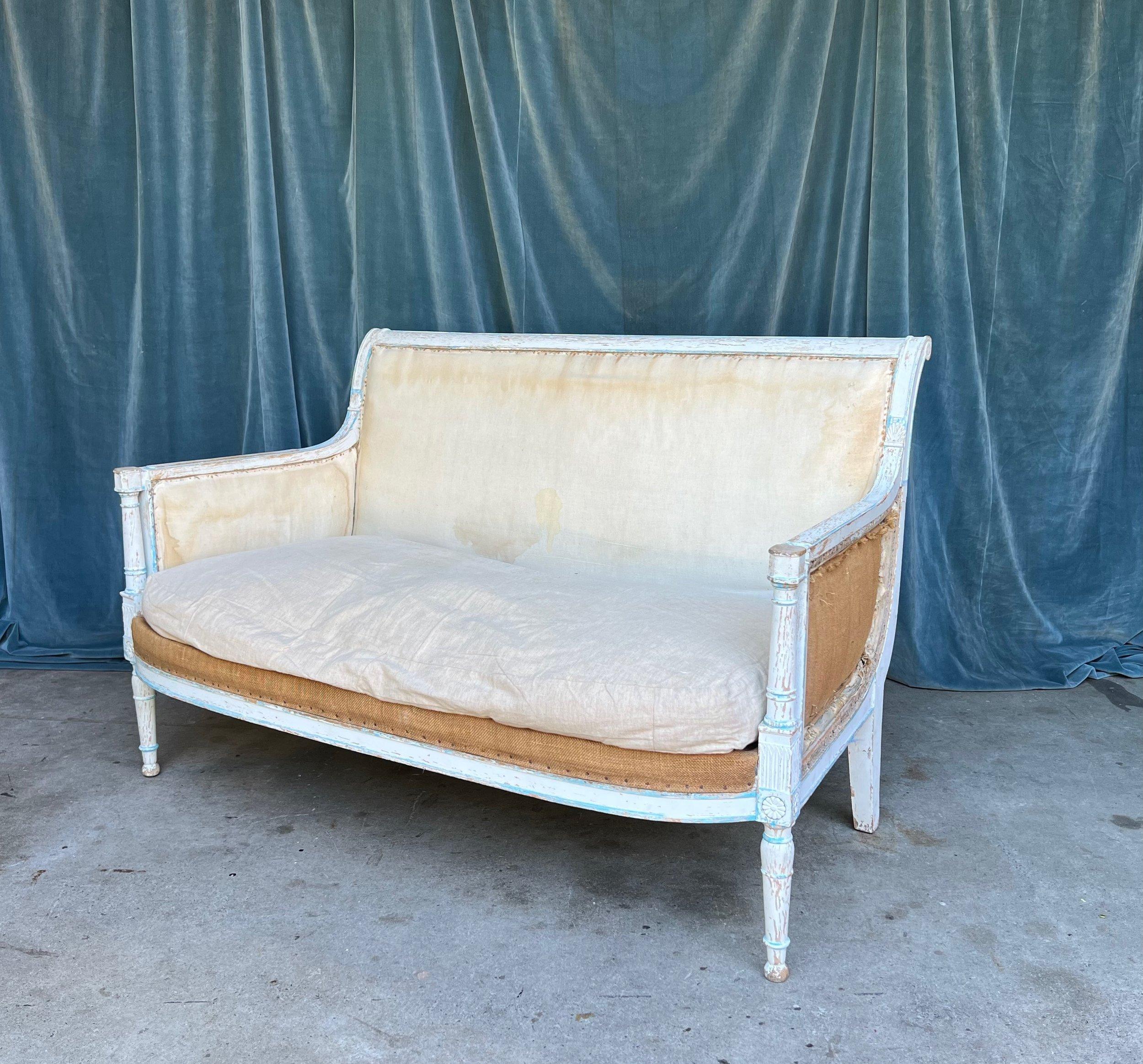 This stunning French 19th century settee, styled in the Directoire manner, is a testament to timeless elegance. The wooden frame, still bearing remnants of its original blue-painted decoration on a white patina, tells an enduring tale of aesthetics