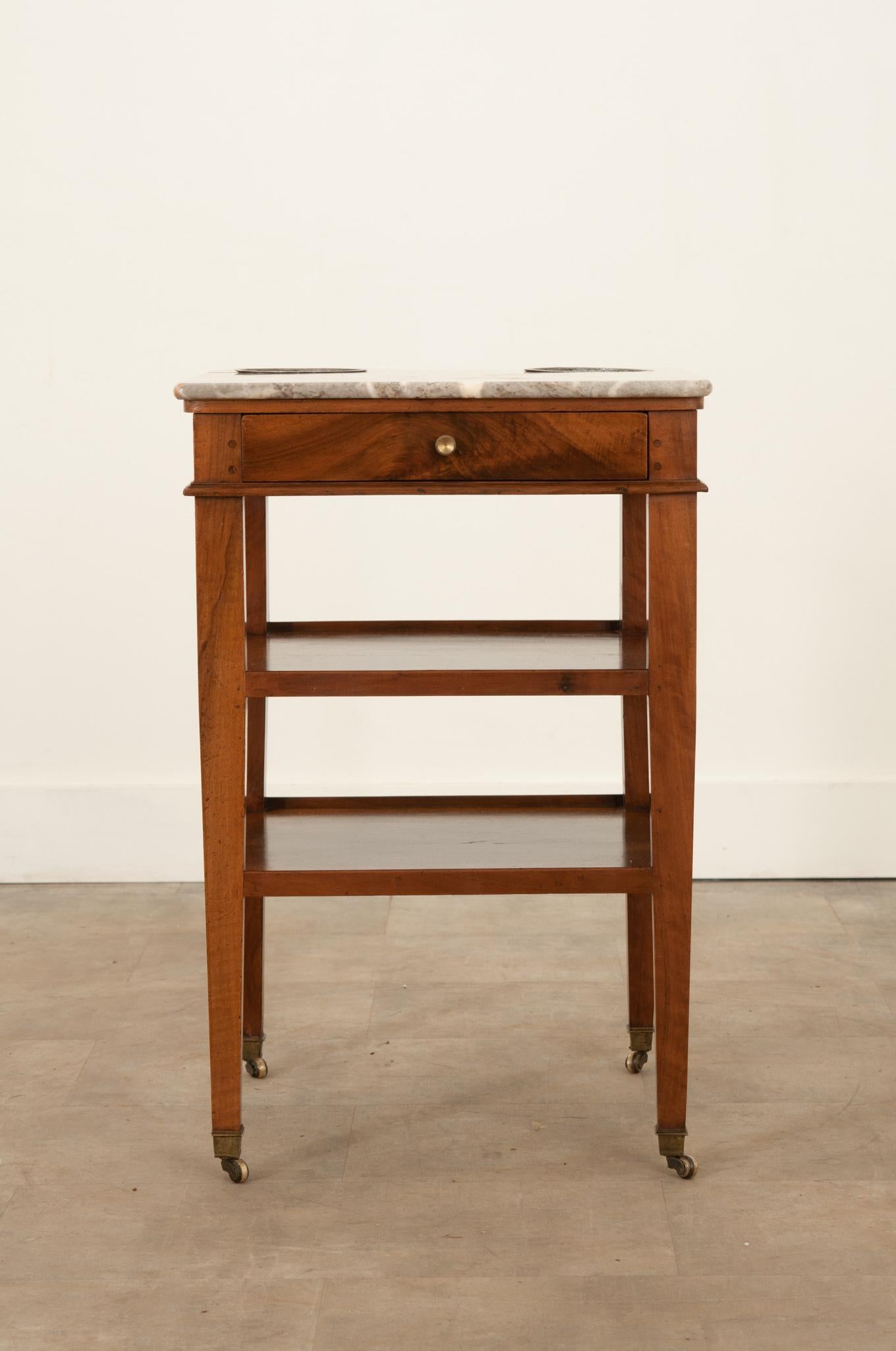 This handsome Directoire rafraichissoir adds a unique touch to any space. The small table is used to chill and serve champagne and other wines that are to be served cold. Custom steel cups are inset into a colorful marble top. The walnut has aged