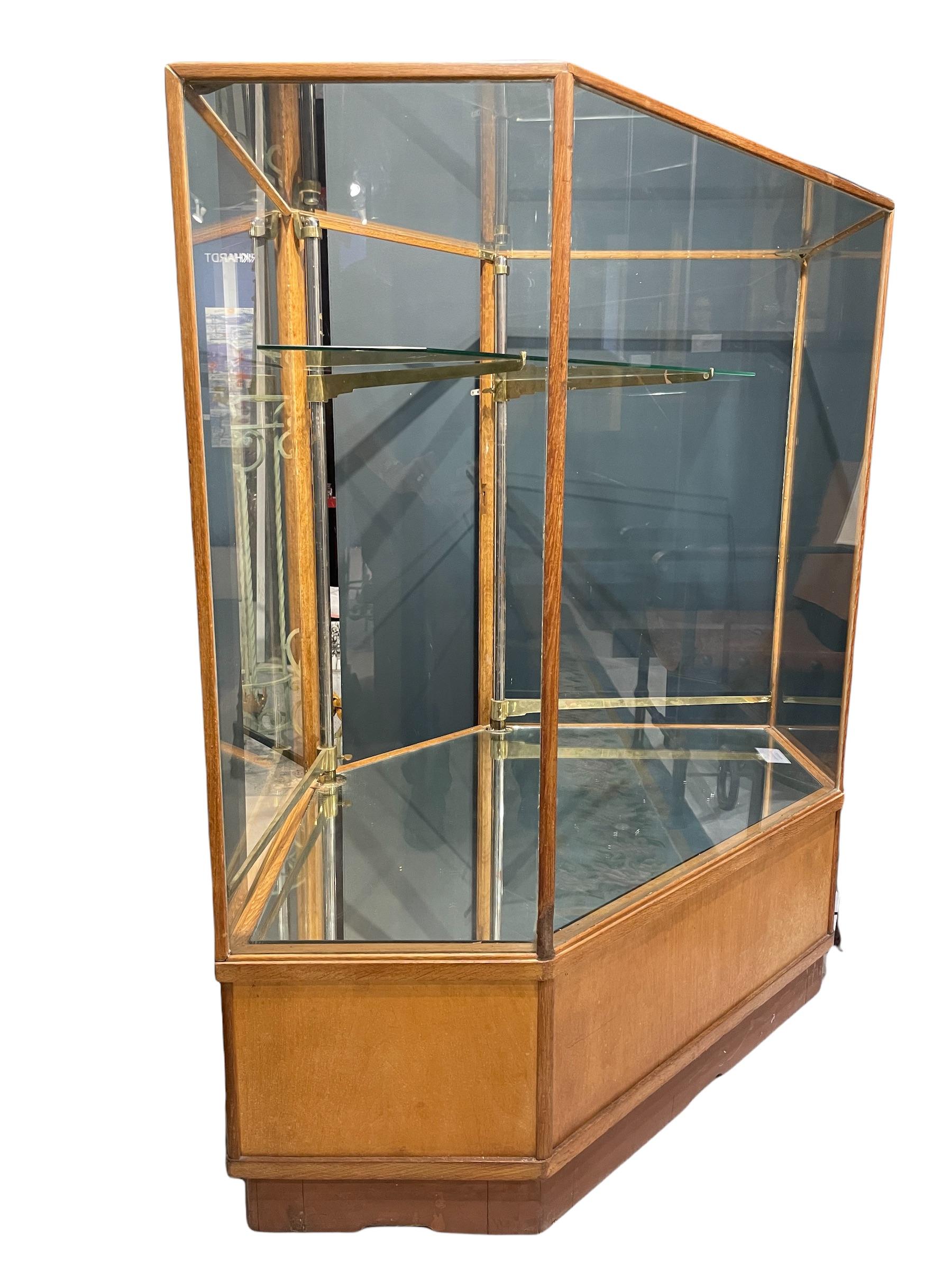 Hexagonal corner cabinet from a Parisian art gallery, this elegant vitrine is glazed on six sides on a wooden base. A practical and easy system allows adjusting the height of the two glass shelves with an intelligent brass mechanism—mirrored glass