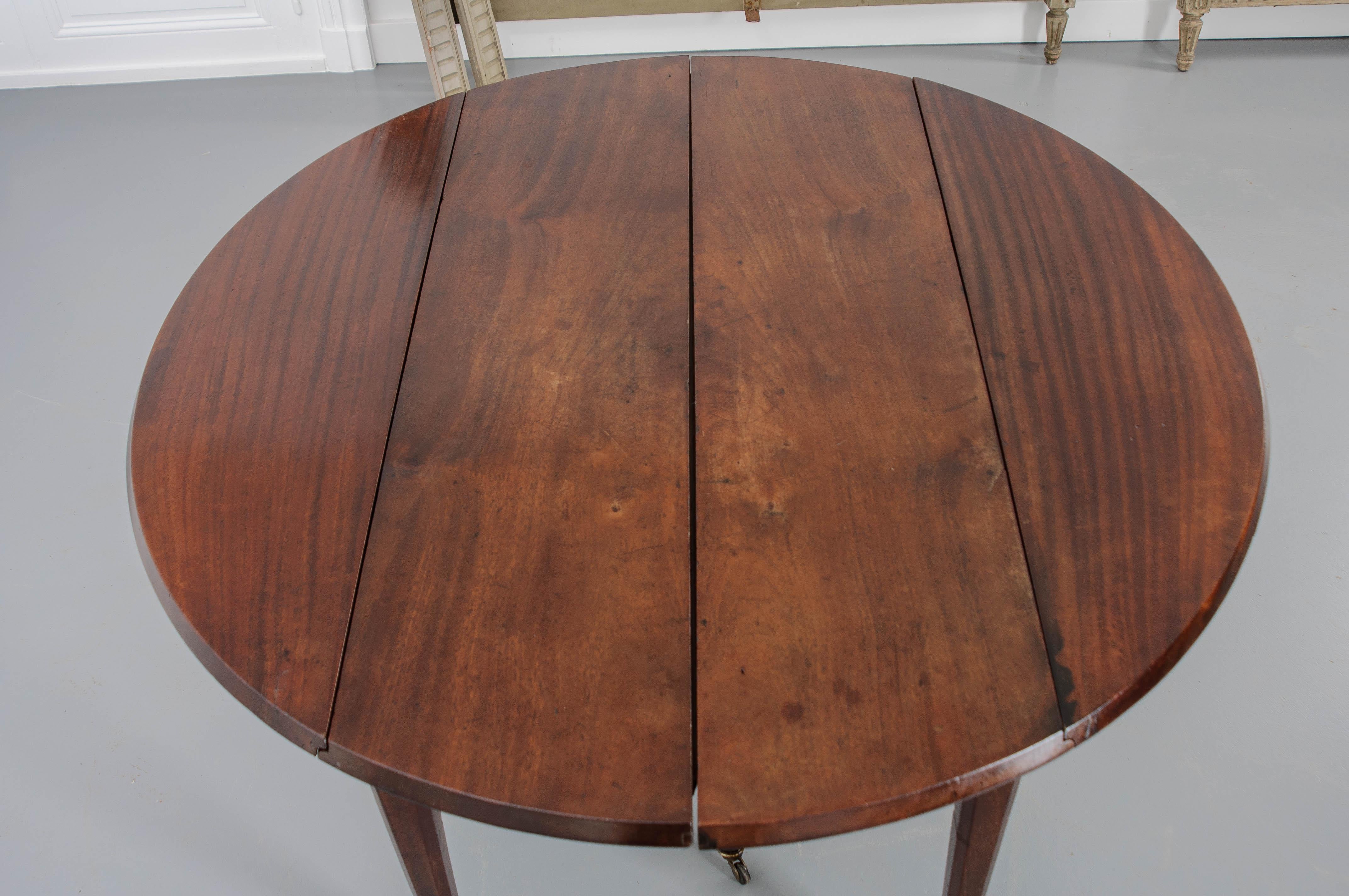 A beautiful French drop leaf dining table. The top sits over a simple apron supported with four tapered legs on sabot feet with brass casters. Each drop leaf has a wood support that pulls out from under the table. The dimensions of the tables with