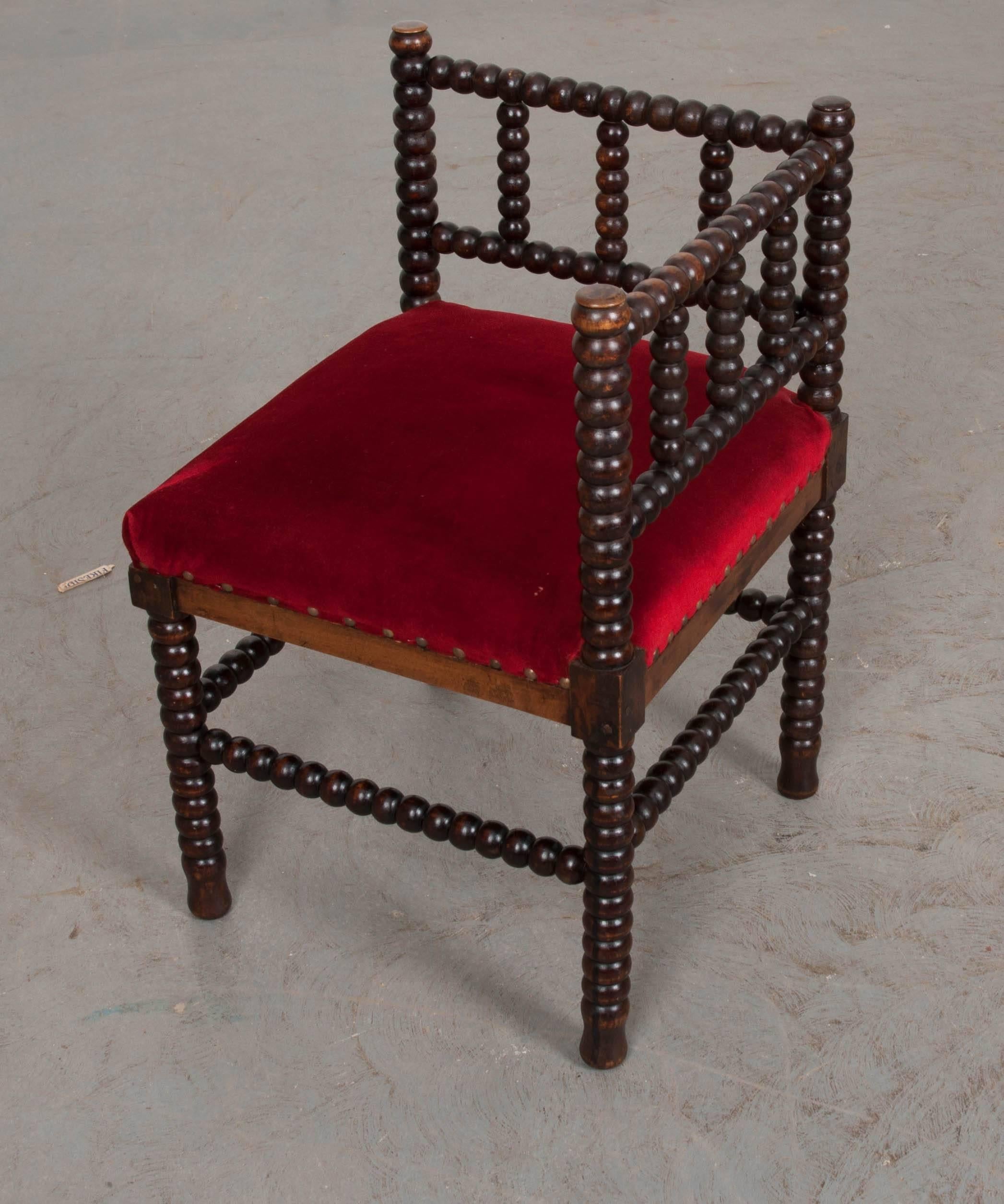 A fabulous bobbin turned, ebonized, corner seat from 19th century France. This little chair has been finished in a magnificently worn ebony that envelopes the turned, hardwood rails that make up the seat. It is upholstered in a vivid red velvet that