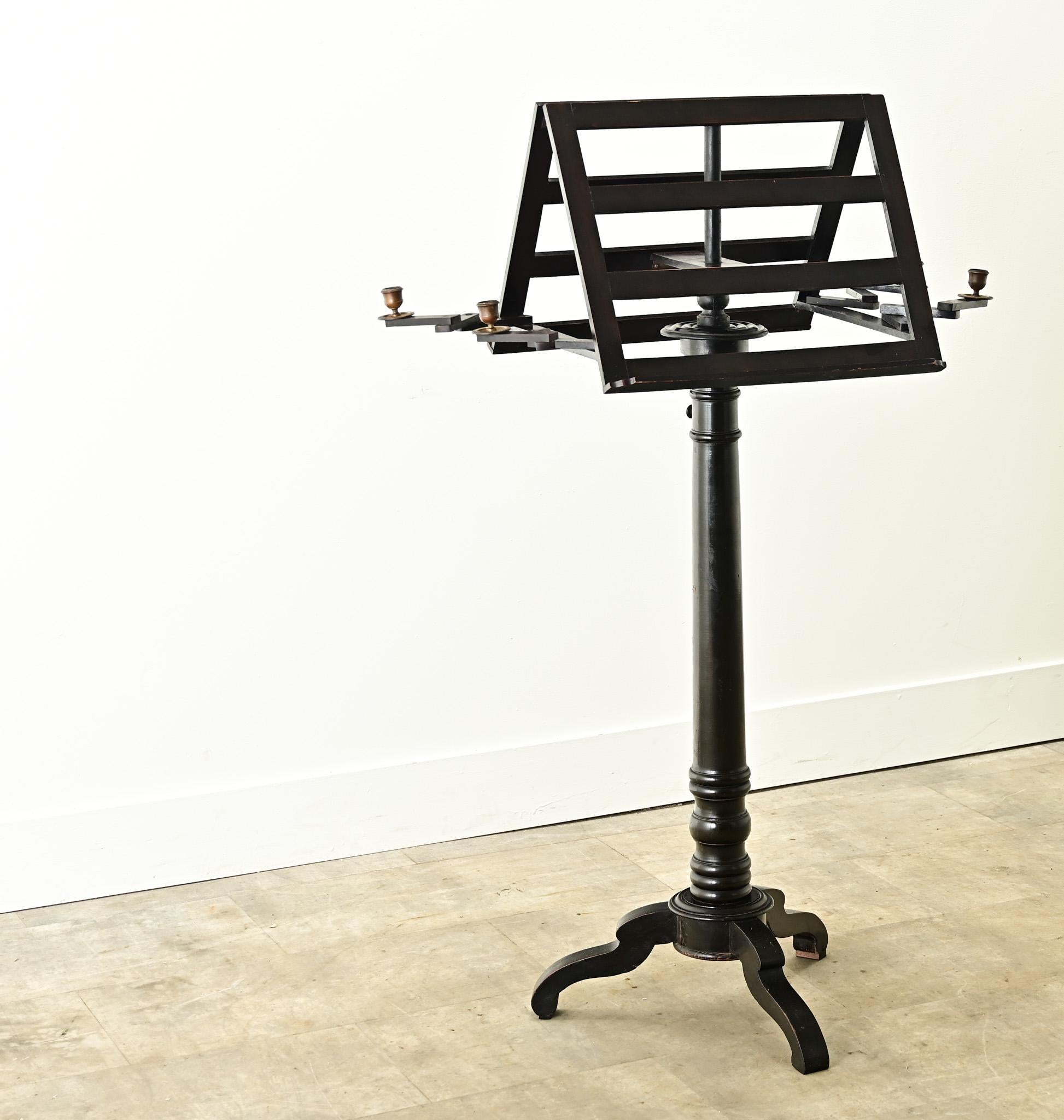 A French ebonized duet stand made in the 1800’s. This antique was built for duet performances with back to back sheet music stands and adjustable brass candle holders. The functional stand is raised on a carved and turned column form base with three