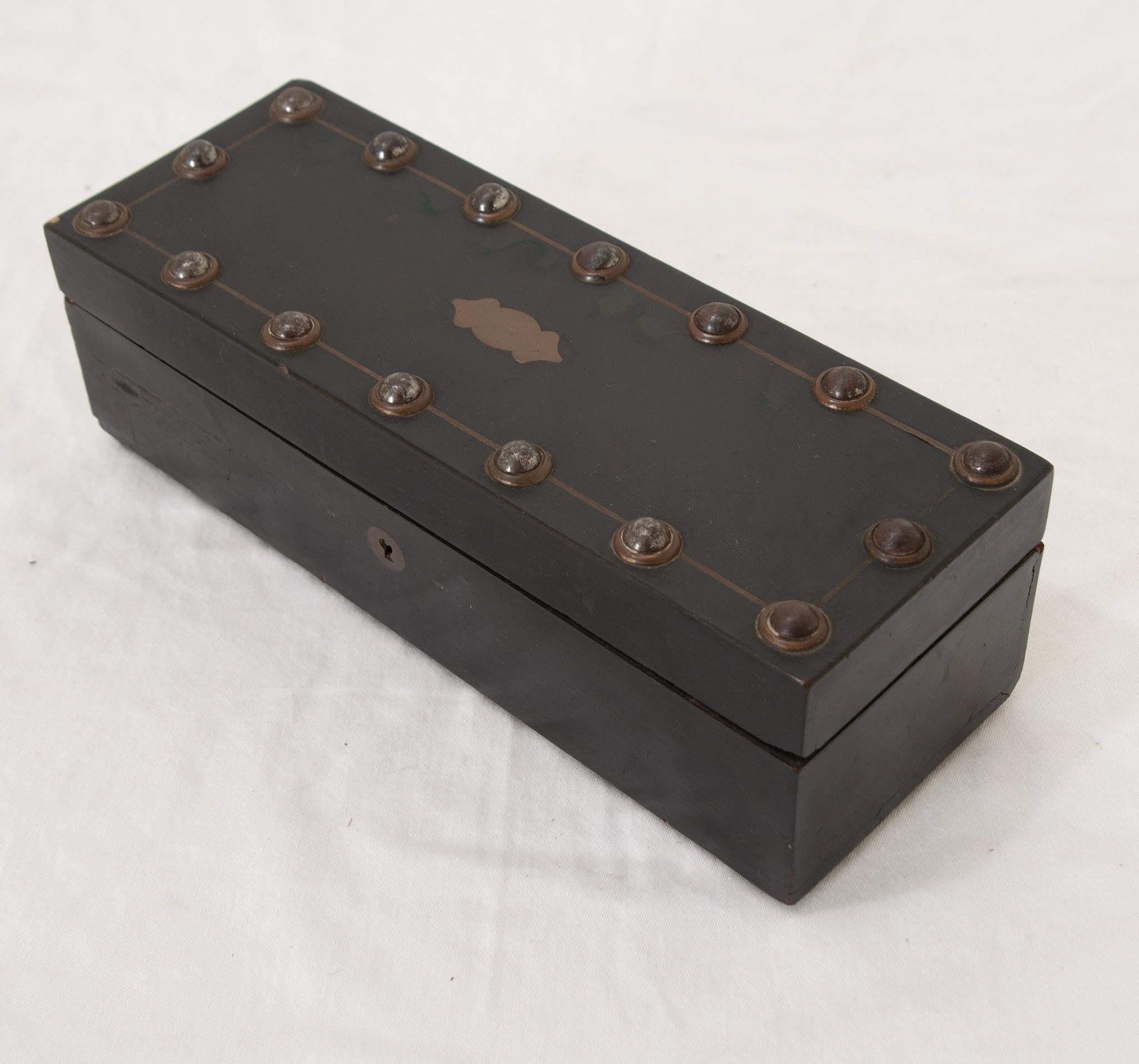A French 19th Century glove box opening on brass hinges to reveal its original fabric lined storage compartments. This handsome box features ebonized wood on its exterior, as well as a large nailhead design and a brass top cartouche. There are clear