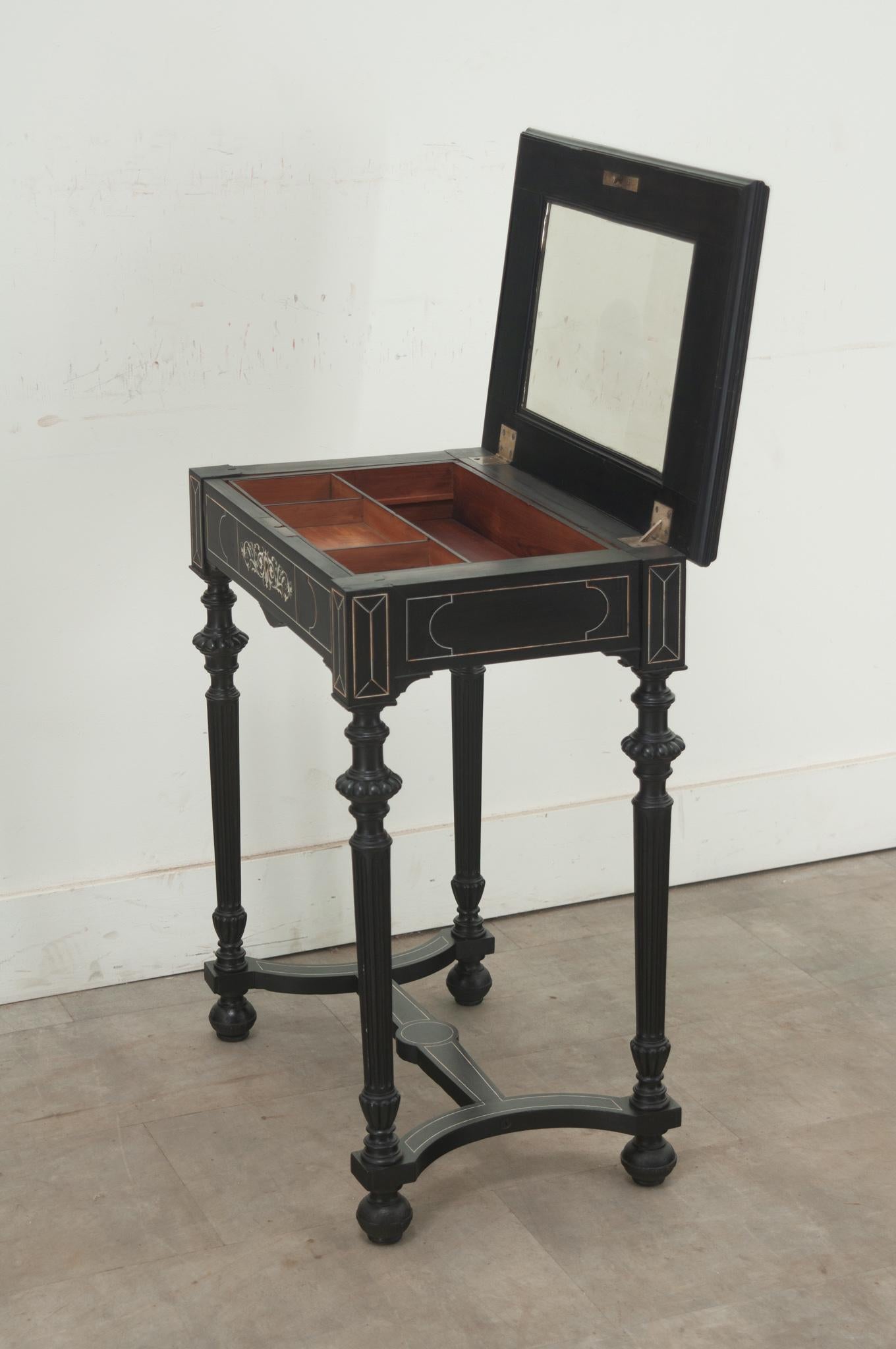 An ebonized and bone inlay petite vanity from the 1800’s, France. The vanity top is connected with brass hinges and opens to reveal an inset mirror. The base is fitted with a removable and sliding tray over a drawer. You’ll find intricate bone inlay