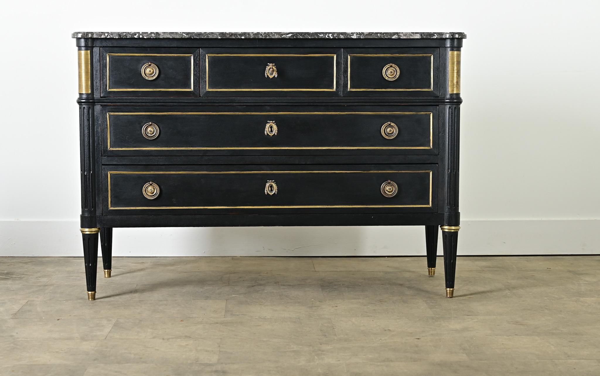 A Louis XVI style, marble-topped commode from France (late 19th century) in bold, ebonized finish that could suit a wide range of decorating tastes today. The St. Anne marble surface is animated by ribbons of light and dark gray veining, shaped at