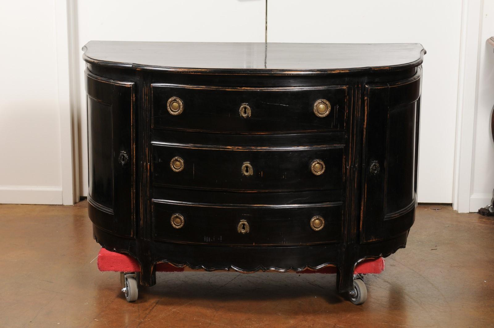 A French ebonized wood demilune credenza from the 19th century with three drawers and side doors. Born in France during the ever-changing 19th century, this French chest cabinet features a semi-circular top with serpentine accents, sitting above