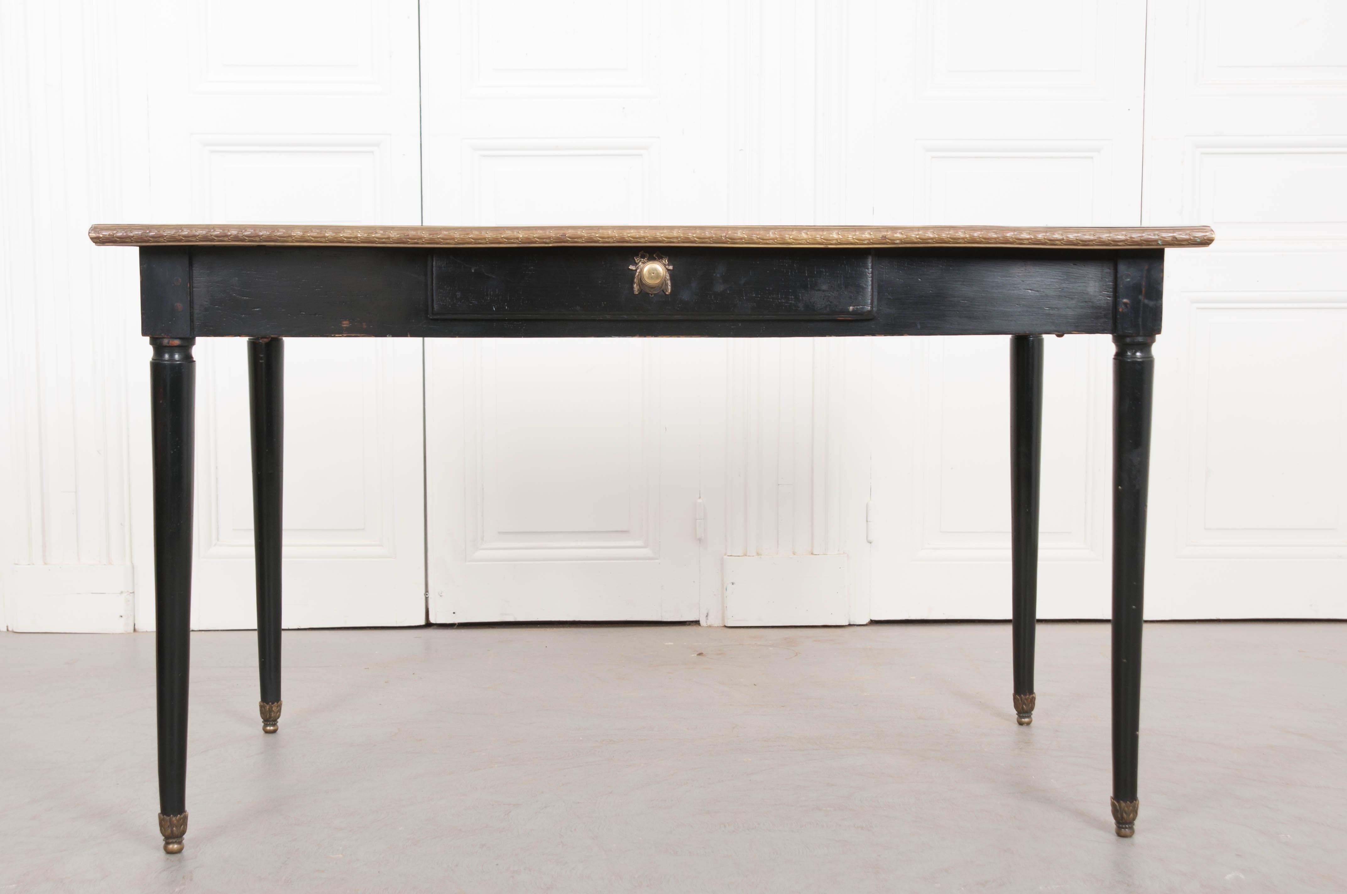 A transitionally styled ebonized writing table from 1880's, France. This refined desk is topped in a fabulous piece of peach-toned, natural colored leather. It is trimmed with gold tooling and embellished with a central diamond-shaped gold-tooled