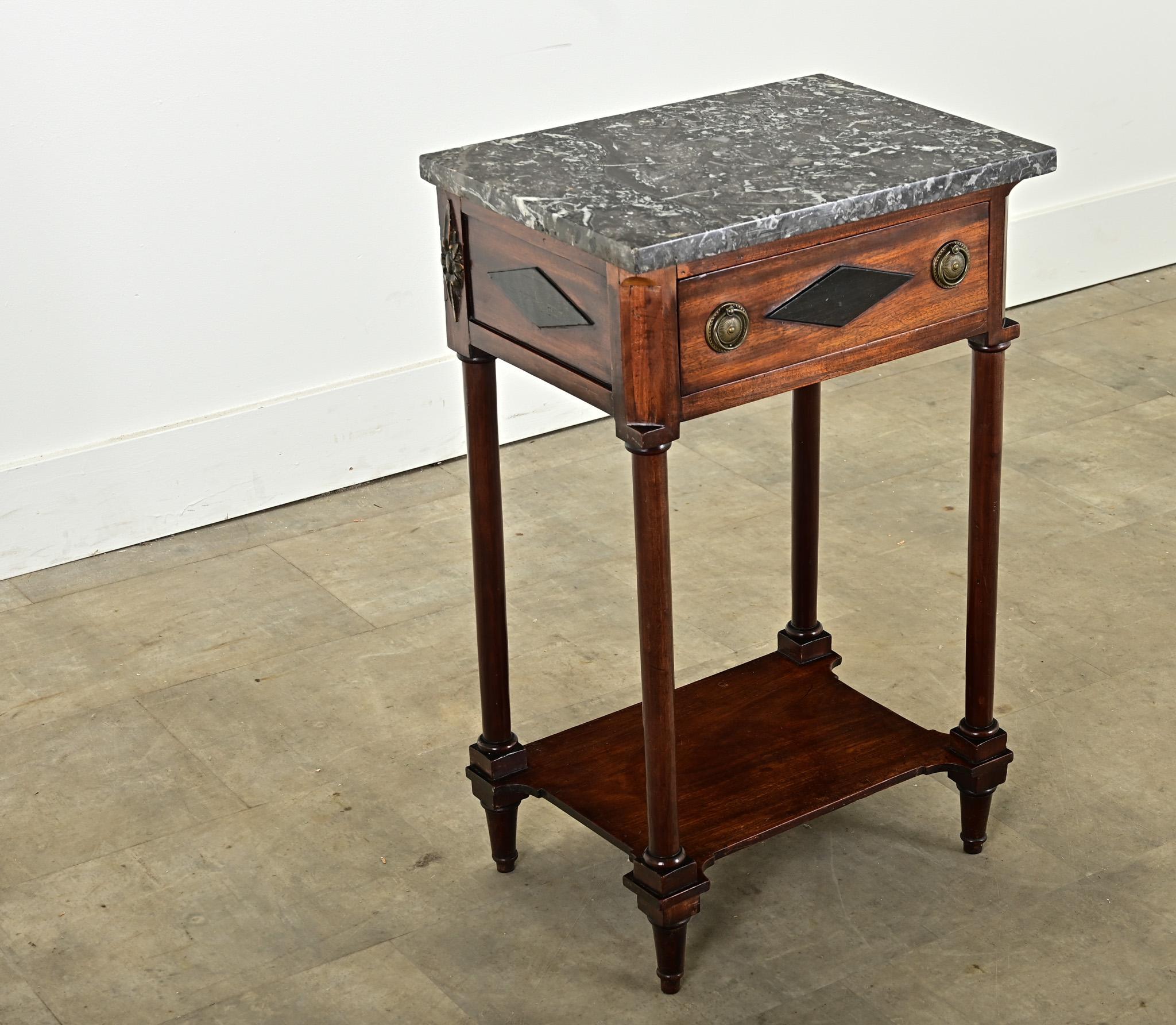 A handsome mahogany French Empire bedside table from the 19th century. This stunning bedside has a beautiful top, made of St. Anne marble, which is in wonderful antique condition. Large ebonized diamond details can be found on the sides and