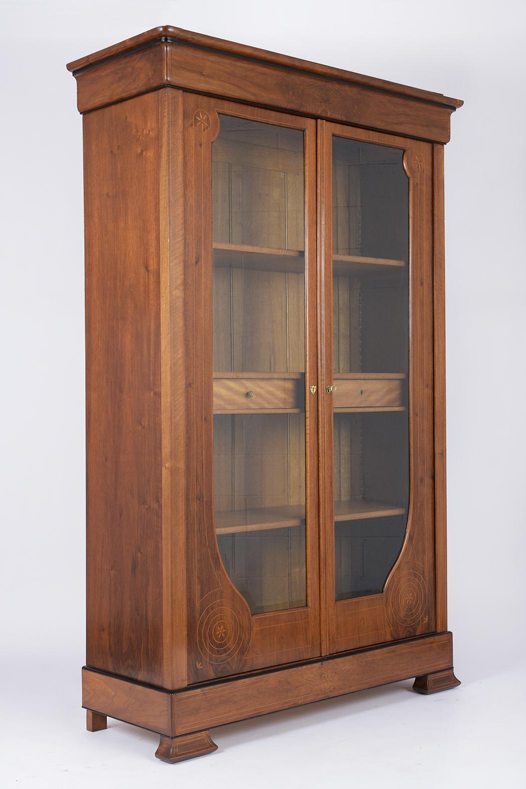 This French 19th century Empire bookcase has been completed restored, is made out of walnut wood with its original walnut color and has a newly waxed and polish patina finish. This bookcase features carved molding along the top/bottom, two large