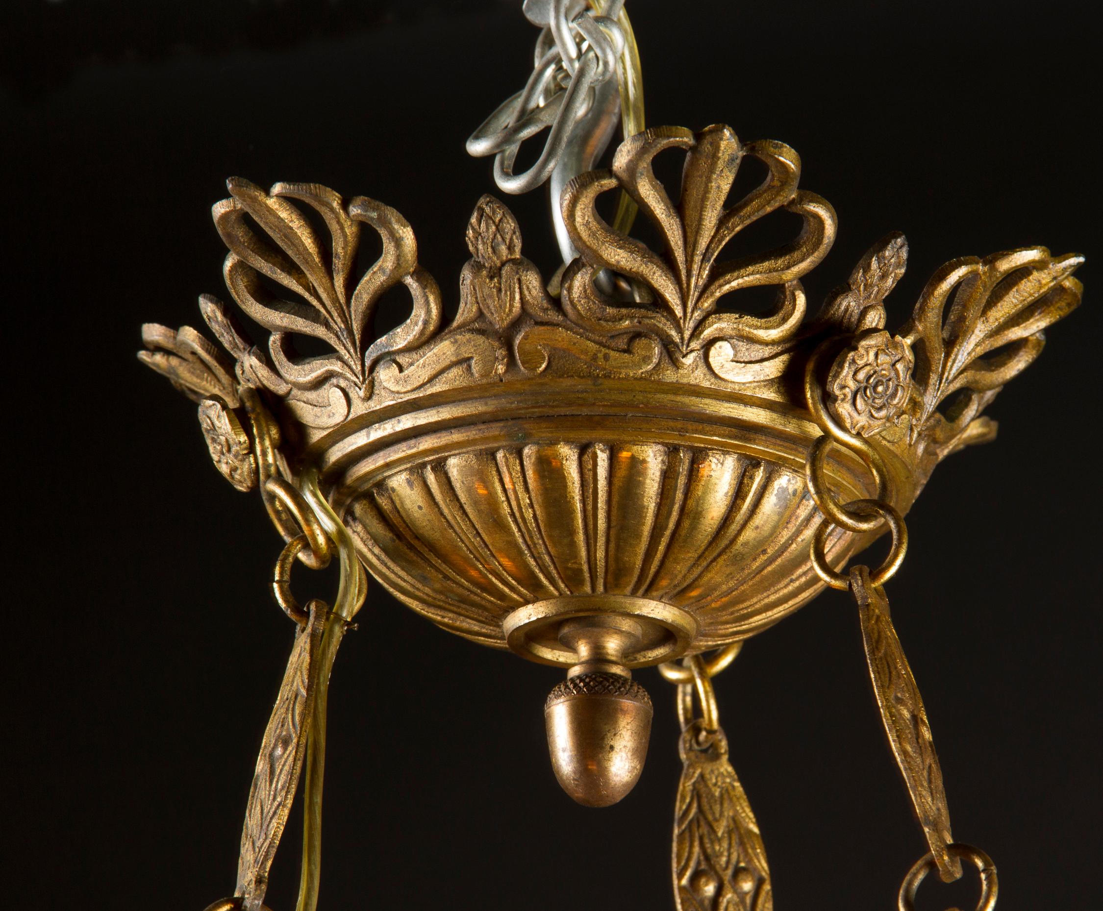 Dieser wunderschöne Empire-Kronleuchter zeichnet sich durch seine verschnörkelte Bronze aus, die sich kontrastreich von einem dunklen Grün abhebt. Das Stück stammt aus dem 19. Jahrhundert, und sein 6-flammiger Sockel hängt an drei Strängen einer