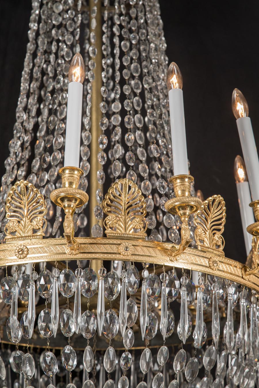 This French Empire chandelier features beautiful bronze accompanied by a plethora of crystals, and dates to the 19th century. Note the oval cut crystals graduating in size from the top to the center ring, the pointed crystals draped at center, below