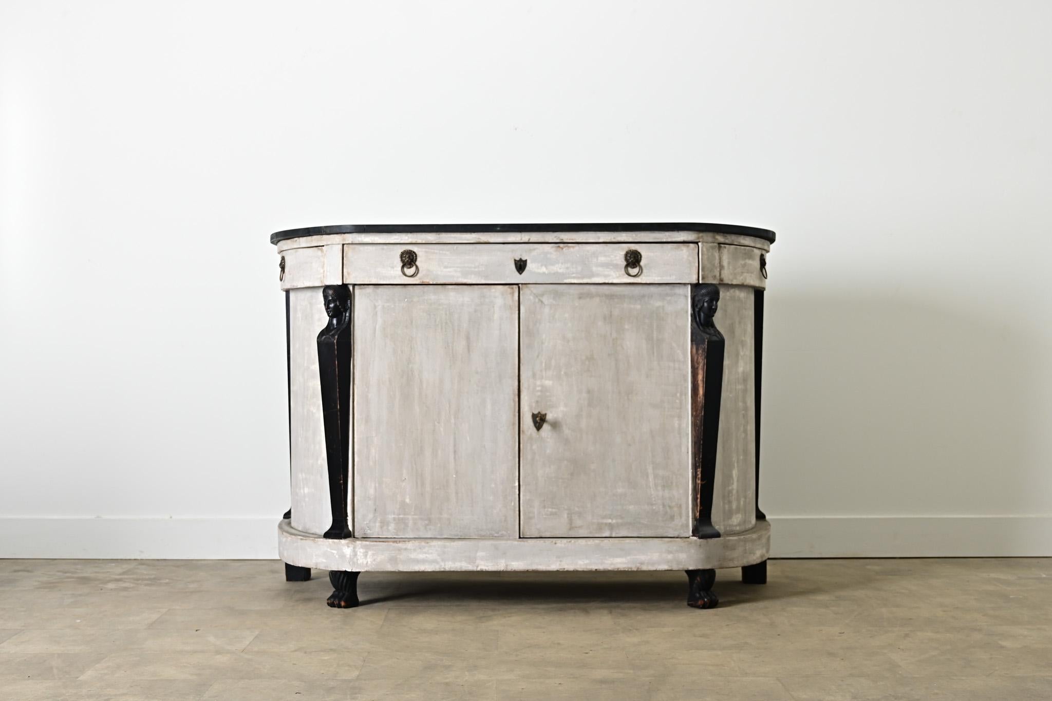A very unique French Empire 19th century buffet, or desserte server, in demilune profile and more recent painted finish of uncertain age. The top surface is a handpainted faux marble that is nearly all black except for delicate wisps of smoky gray