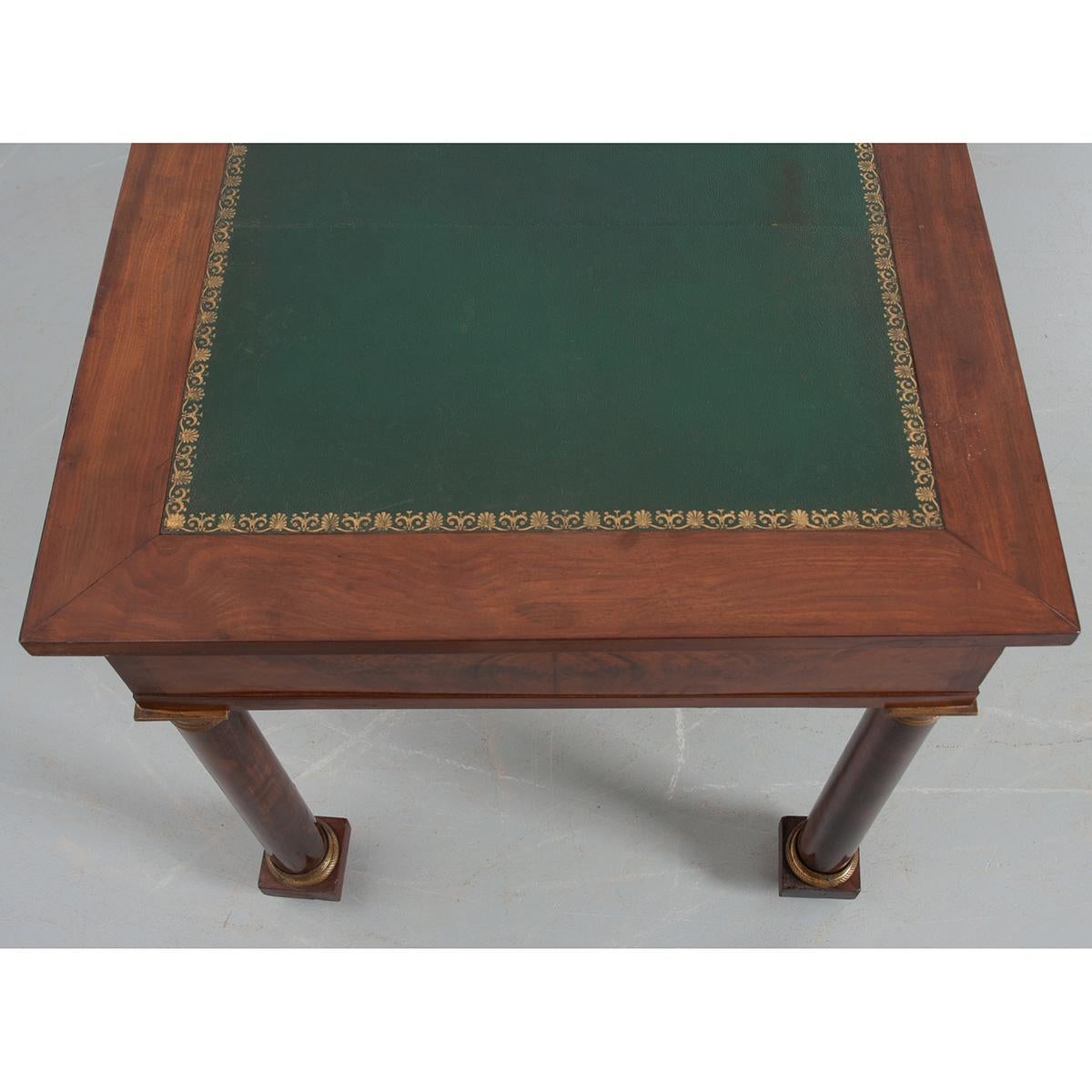 A stately Empire bureau plat with a tooled leather top, c. 1830. The three-piece green leather top has a beautiful gold tooled filigree border and is framed in mahogany. You will find three drawers in the apron; two smaller drawers with brass knobs