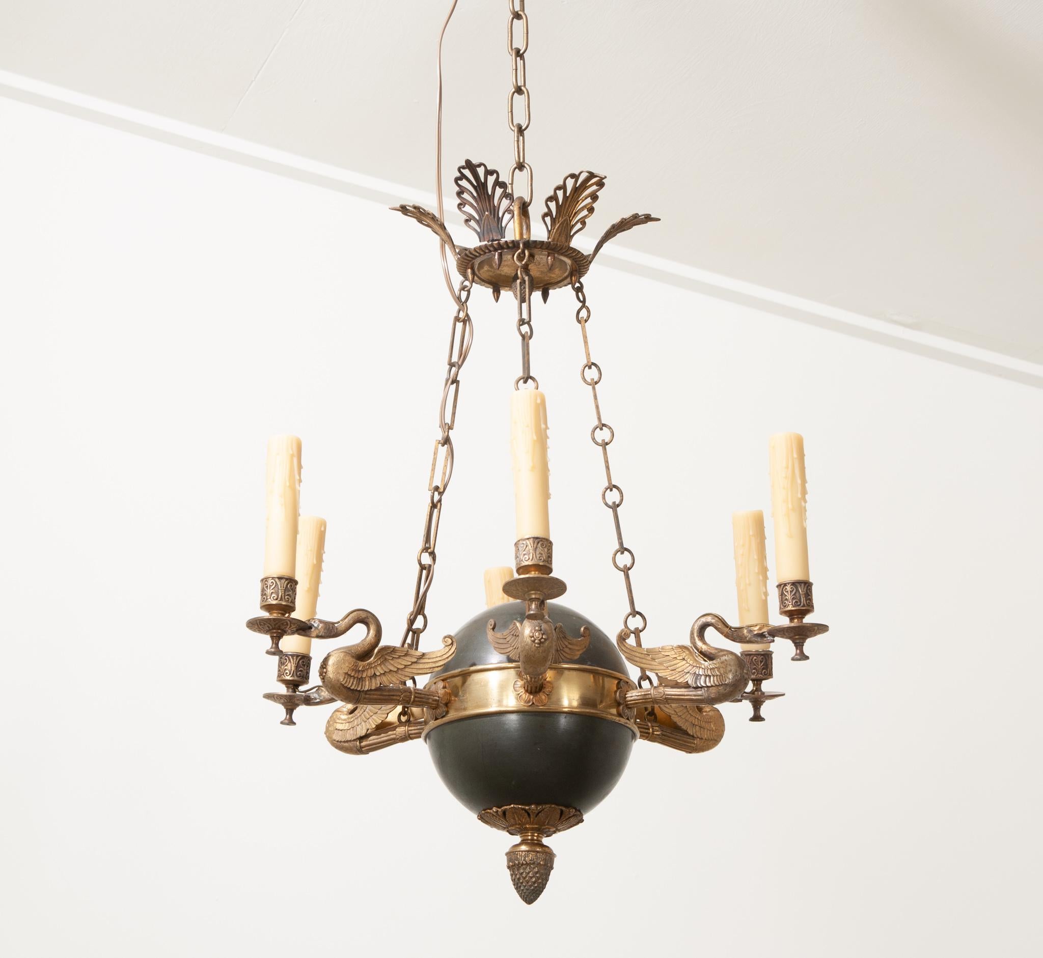 A French 19th Century Empirically styled six arm chandelier that is just as artful as it is functional. Its spherical black brass suspension weight and patinated brass design elements contrast each other wonderfully. The underside of the round