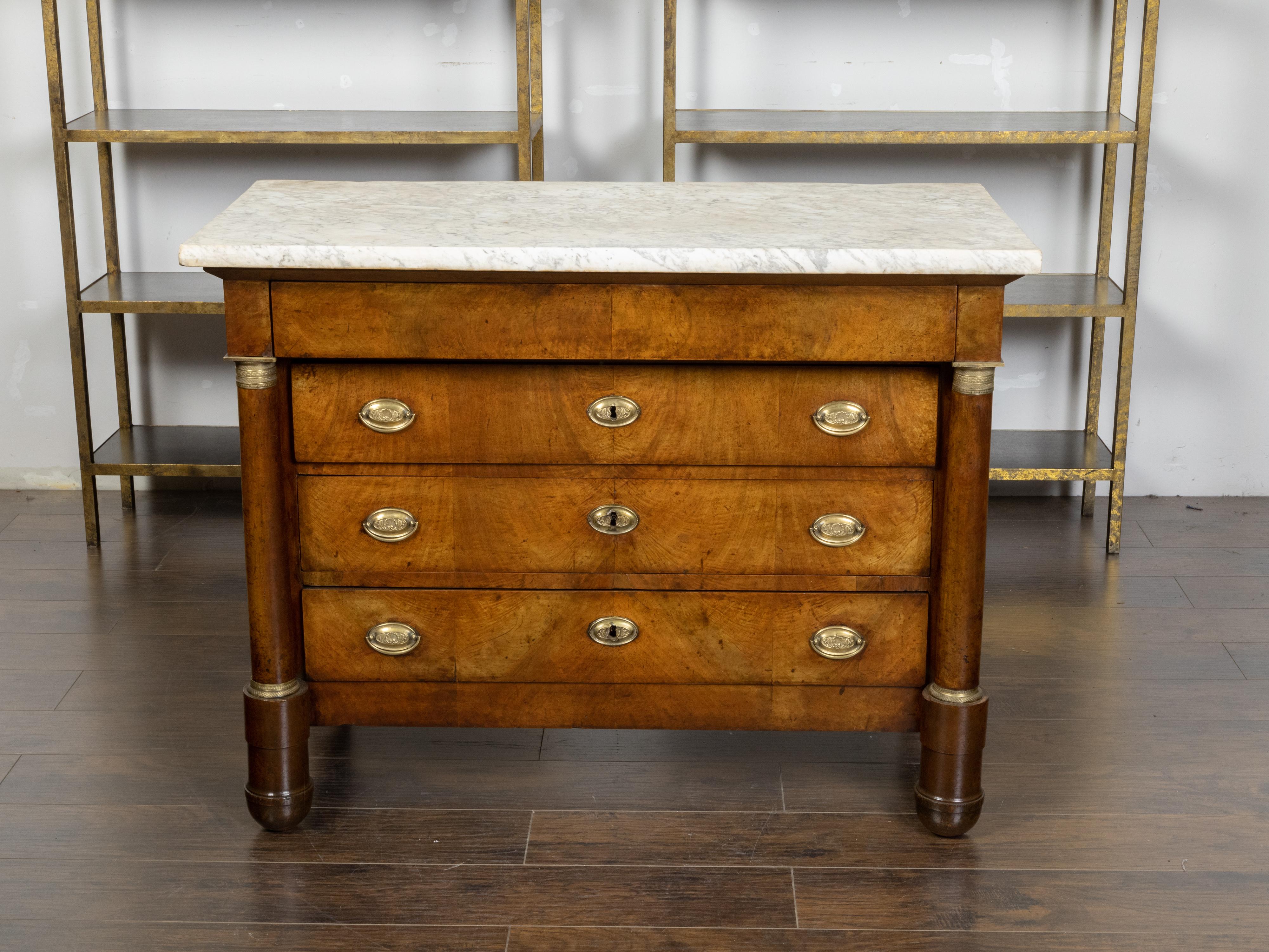 A French Empire commode from the 19th century, with white marble top, four drawers, butterfly veneer, bronze mounts and column-shaped posts. Created in France during the 19th century, this Empire commode features a rectangular white marble top