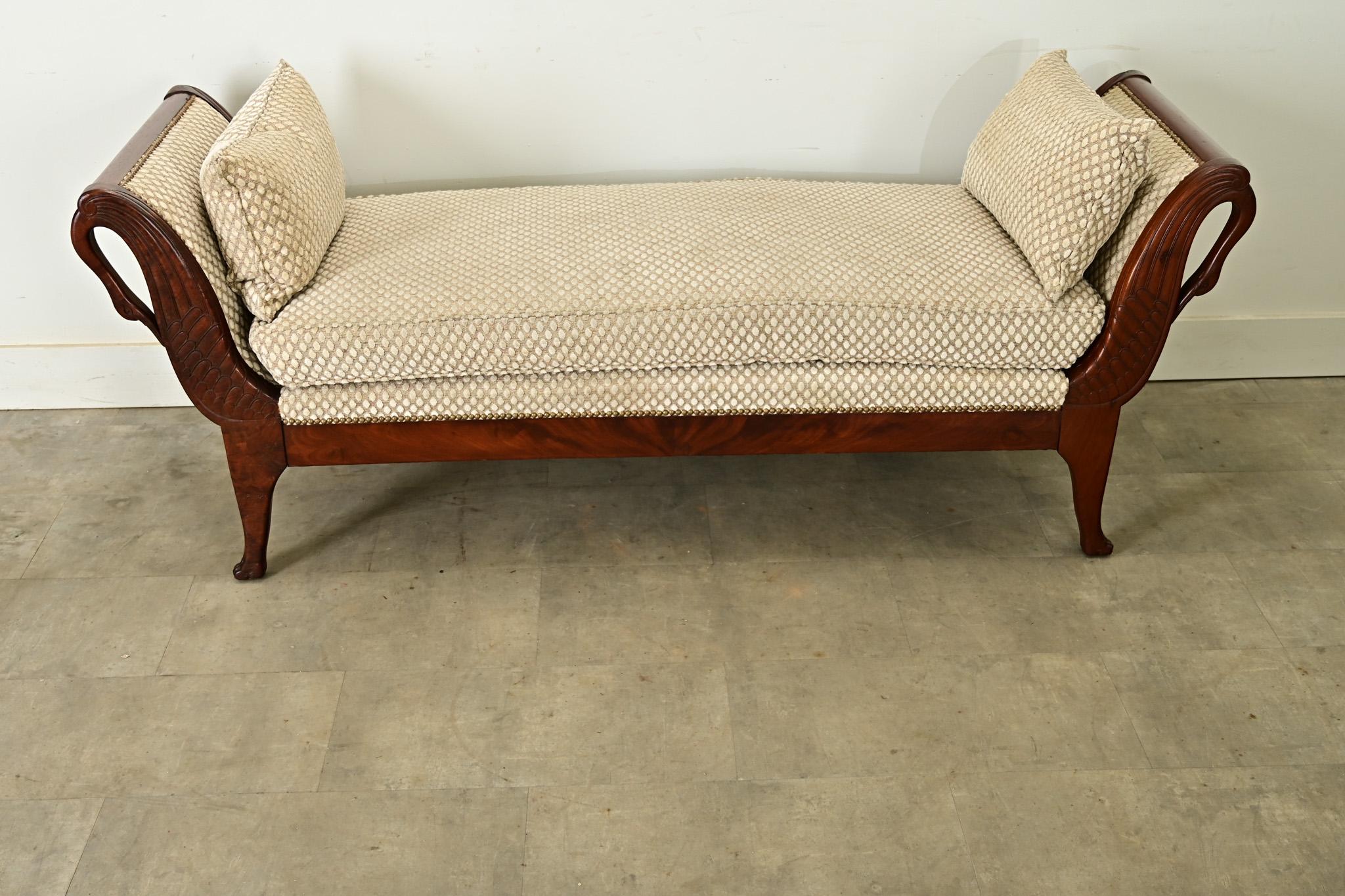 A graceful 19th-century French Empire daybed, expertly carved from solid mahogany with curvaceous swan motif. Featuring a sleigh-like profile and perfectly symmetrical, allowing the piece to float in a living room or complement a bedroom. A dotted