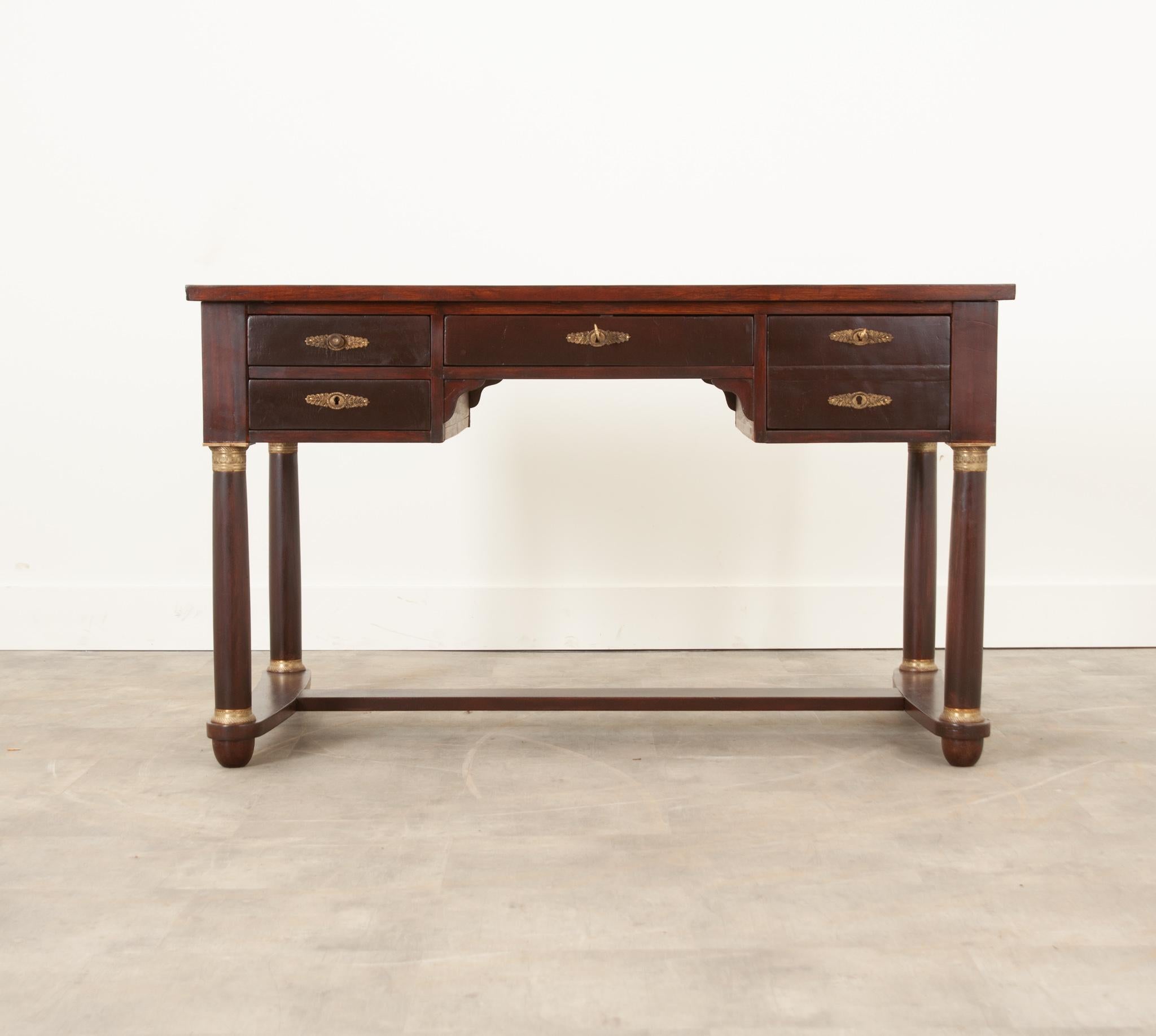 Emanate professionality from behind this stunning Empire-style mahogany desk, made in France during the 1800’s. The desk is topped in beautifully tooled worn gold leather. The desk’s work surface can be enlarged with a pull of either slide that is