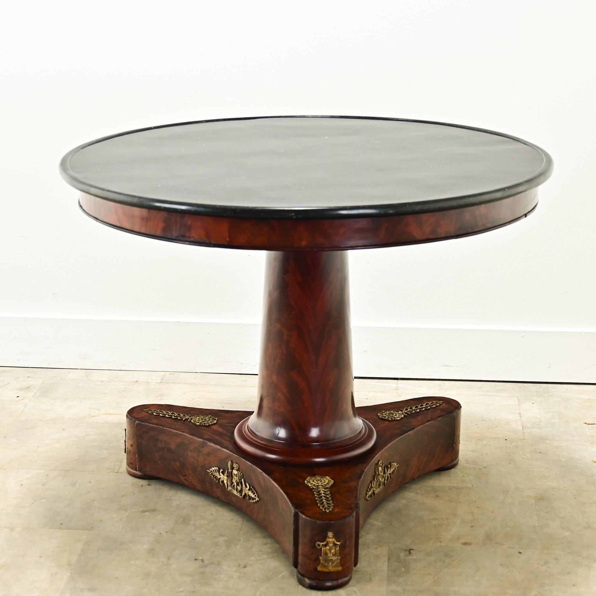 A large French Empire period gueridon from the 1800’s. The original fossil black marble top has been professionally repaired. Its refined mahogany base has a simple apron above a column form center pedestal and three concave legs with neoclassical