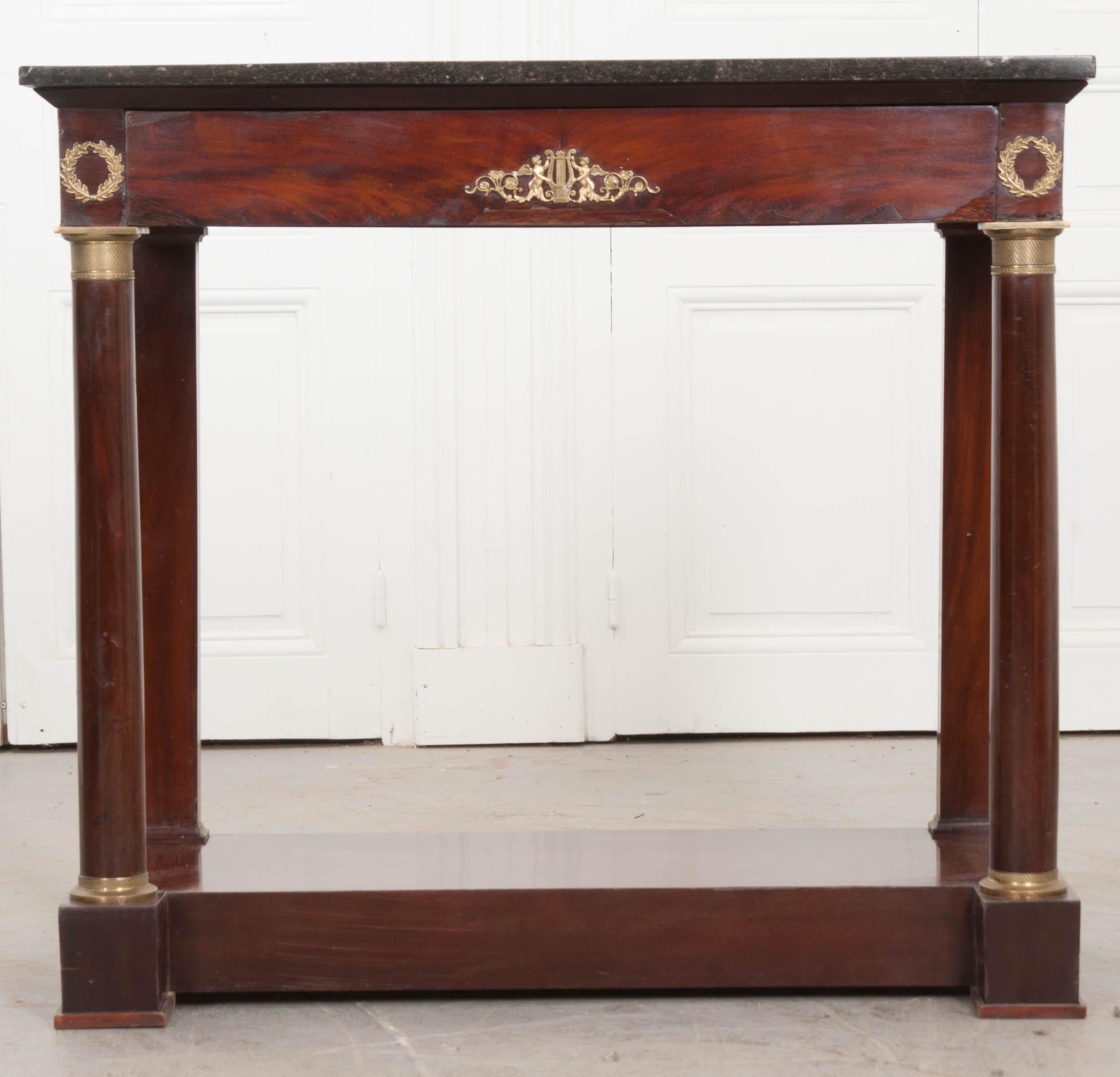 This elegant Empire-style mahogany console is from France, circa 1880, and features a charcoal-grey marble top with delicate white veining, over an apron with a central ormolu mount depicting a lyre flanked by a pair of cherubs, as well as “laurel