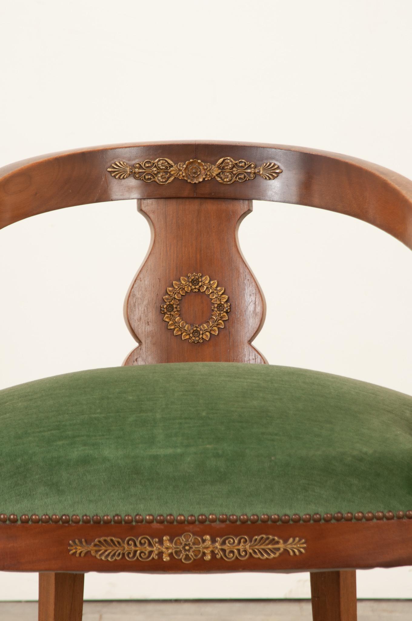 The mahogany frame of this Empire chair has gained a fine patina and is embellished with fantastic ormolu throughout the design. A combination of rosette and palm motifs soften the stalwart design. The green mohair velvet upholstery has held up well