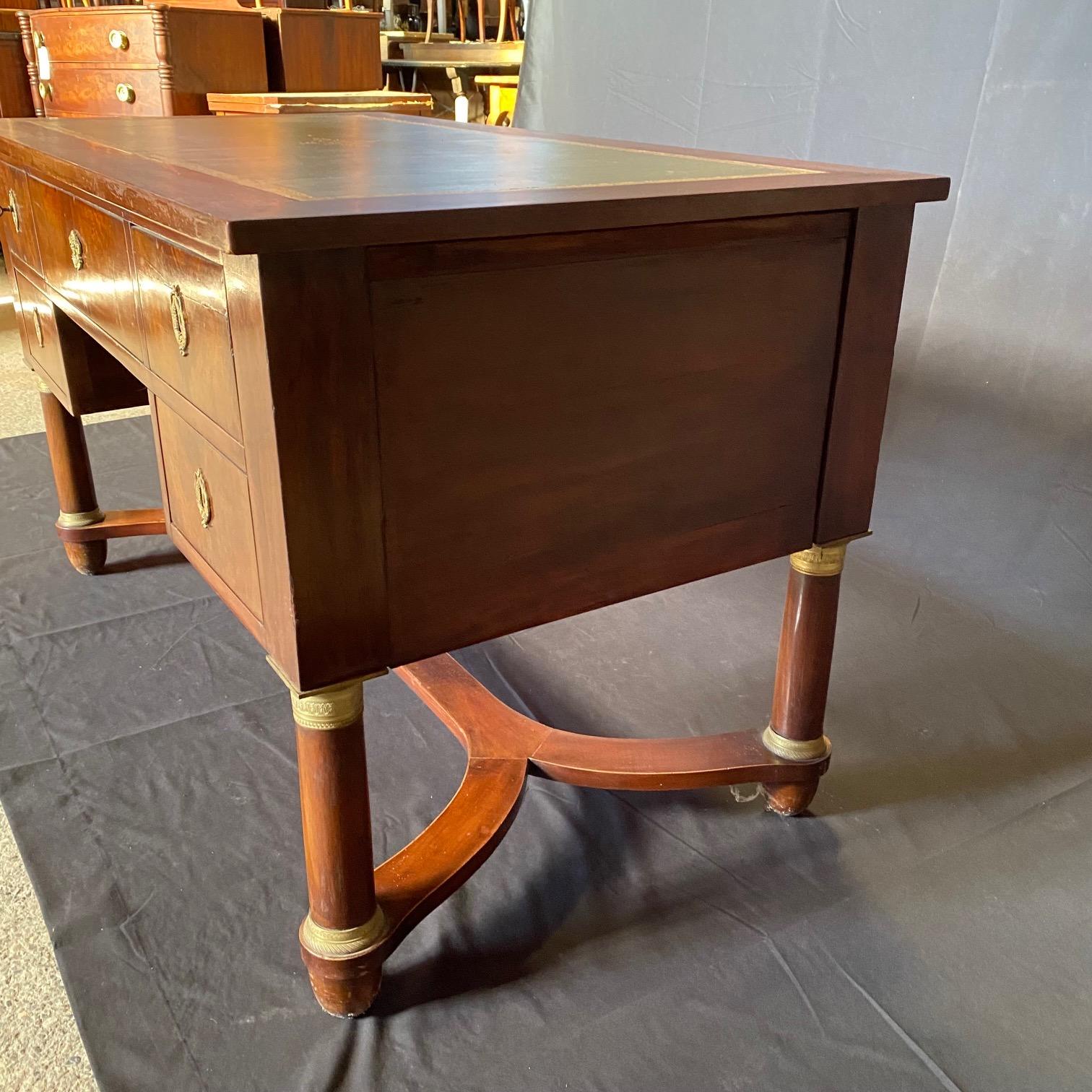 Elegant dual-sided 1880s French Empire style pedestal leg desk featuring the original rectangular gold embossed green leather top in good condition. Top sits on turned trestle legs with gilt bronze accents and stretcher. The single center drawer has